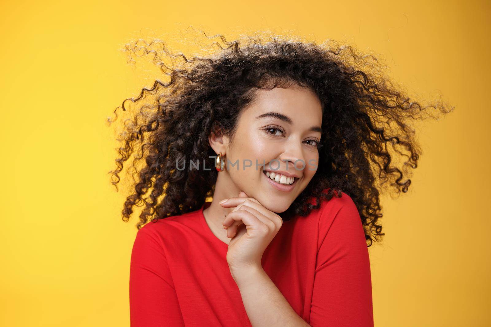 Romance, women and beauty concept. Portrait of tender and gentle pretty woman with curly hair flying in air as she turning head and smiling sensually, flirting with camera touching chin.
