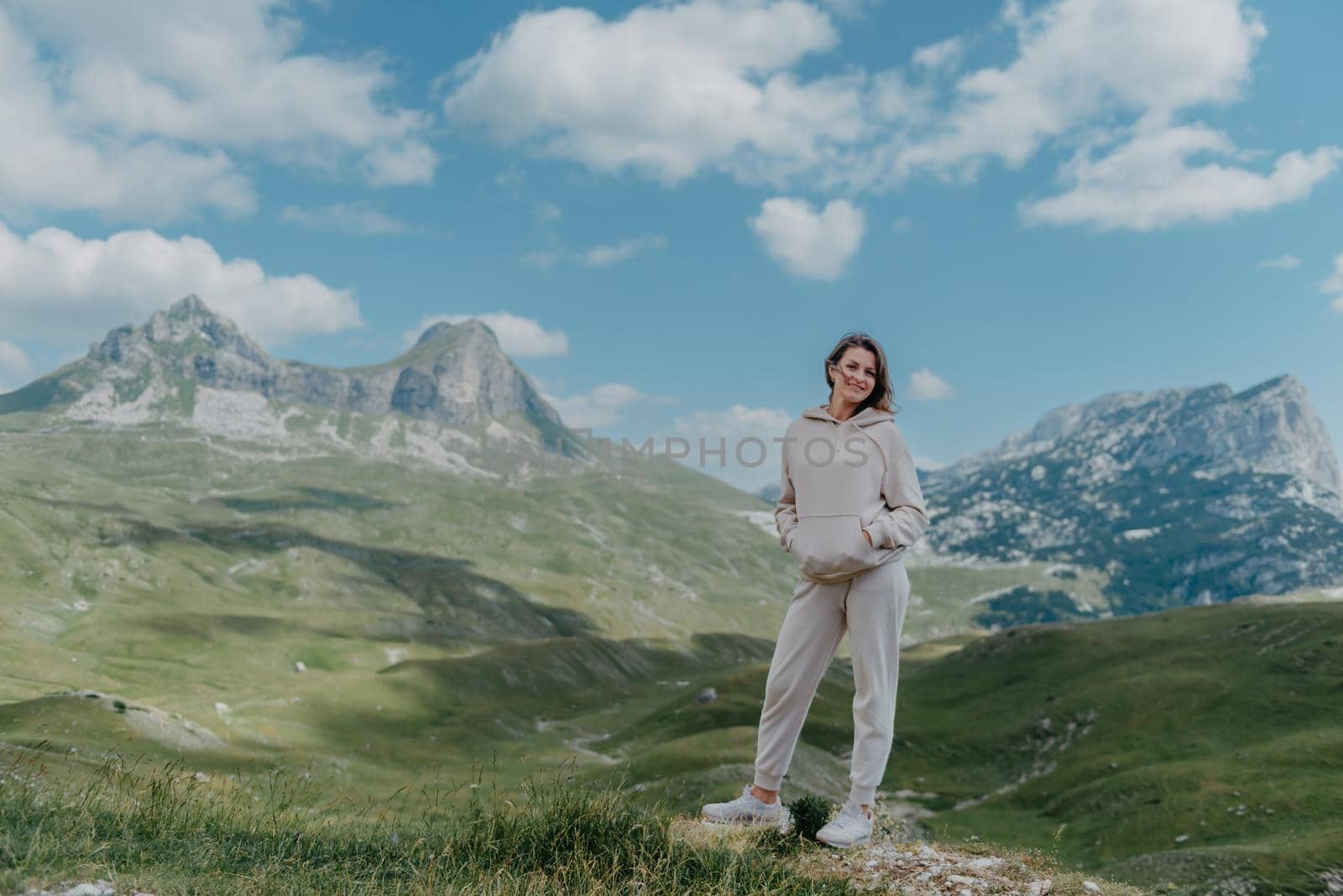 Hiker tourist girl standing on top of the mountain and enjoying valley view. Happy woman with her arms outstretched, freedom and happiness, achievement in mountains.