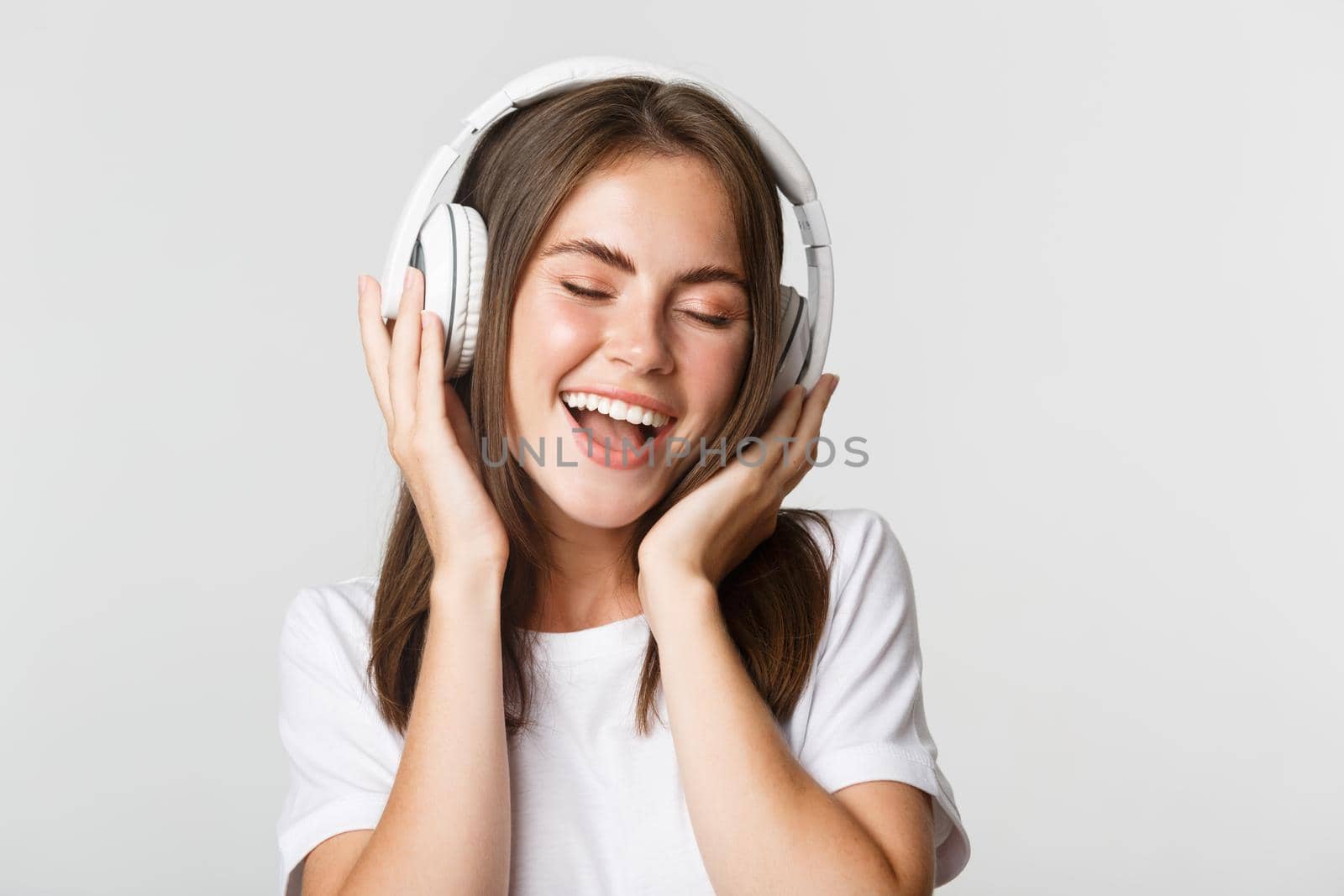 Close-up of attractive happy woman listening music in wireless headphones, singing along.