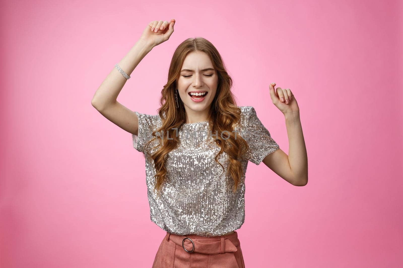Attractive glamour female dancing dance-floor having fun rase hands up sky close eyes singing along songs enjoying awesome party cool music, wearing glittering blouse trendy skirt, pink background.
