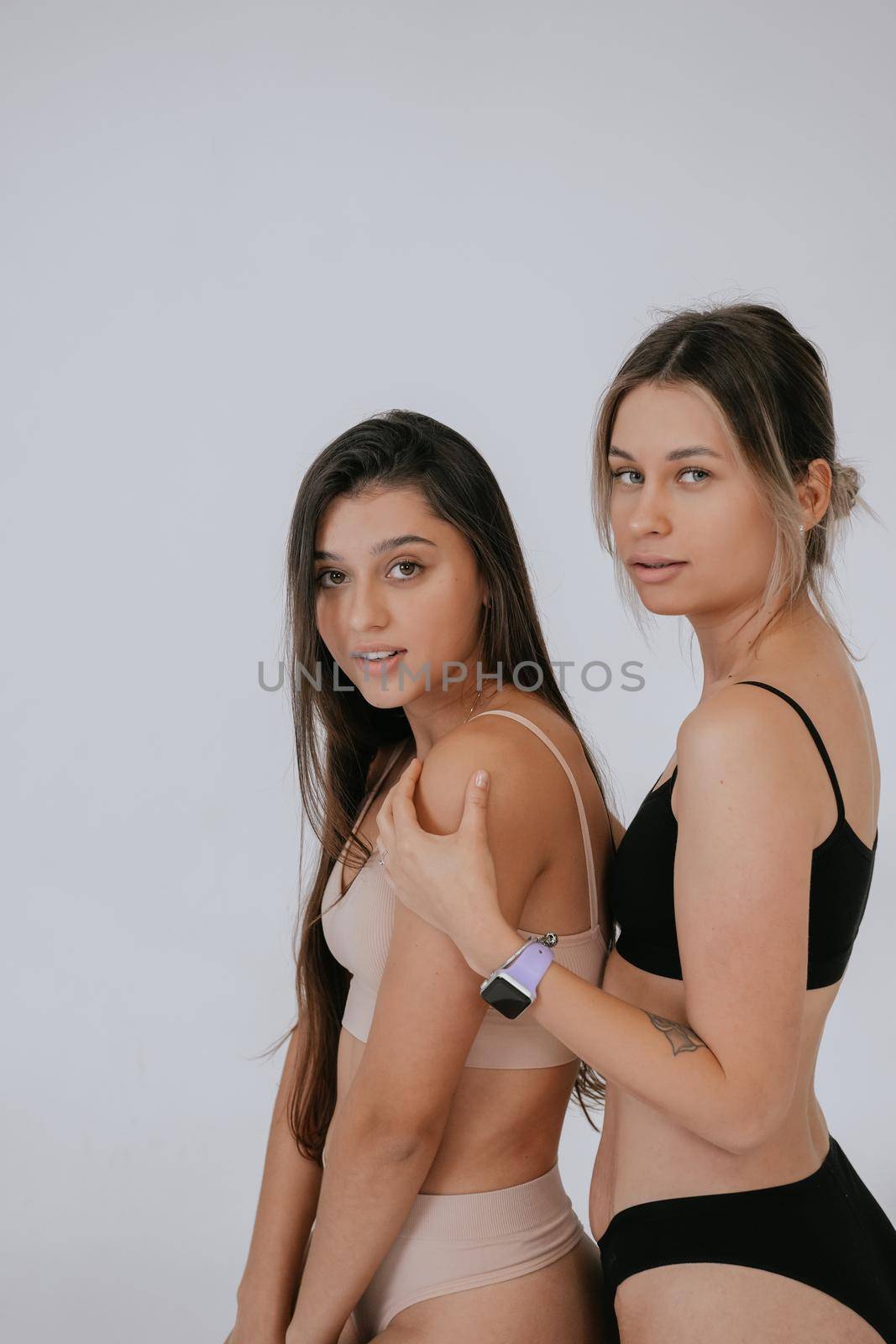 Two diverse models wearing underwear stand side to the camera , enjoying time together, look at camera having smile and natural unique beauty