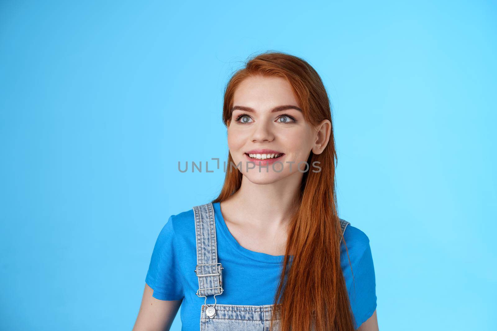 Dreamy creative cheerful redhead woman contemplate sky, smiling upbeat, rejoice good summer weather, gaze up happy, grin satisfied, observe interesting promo, stand blue background.