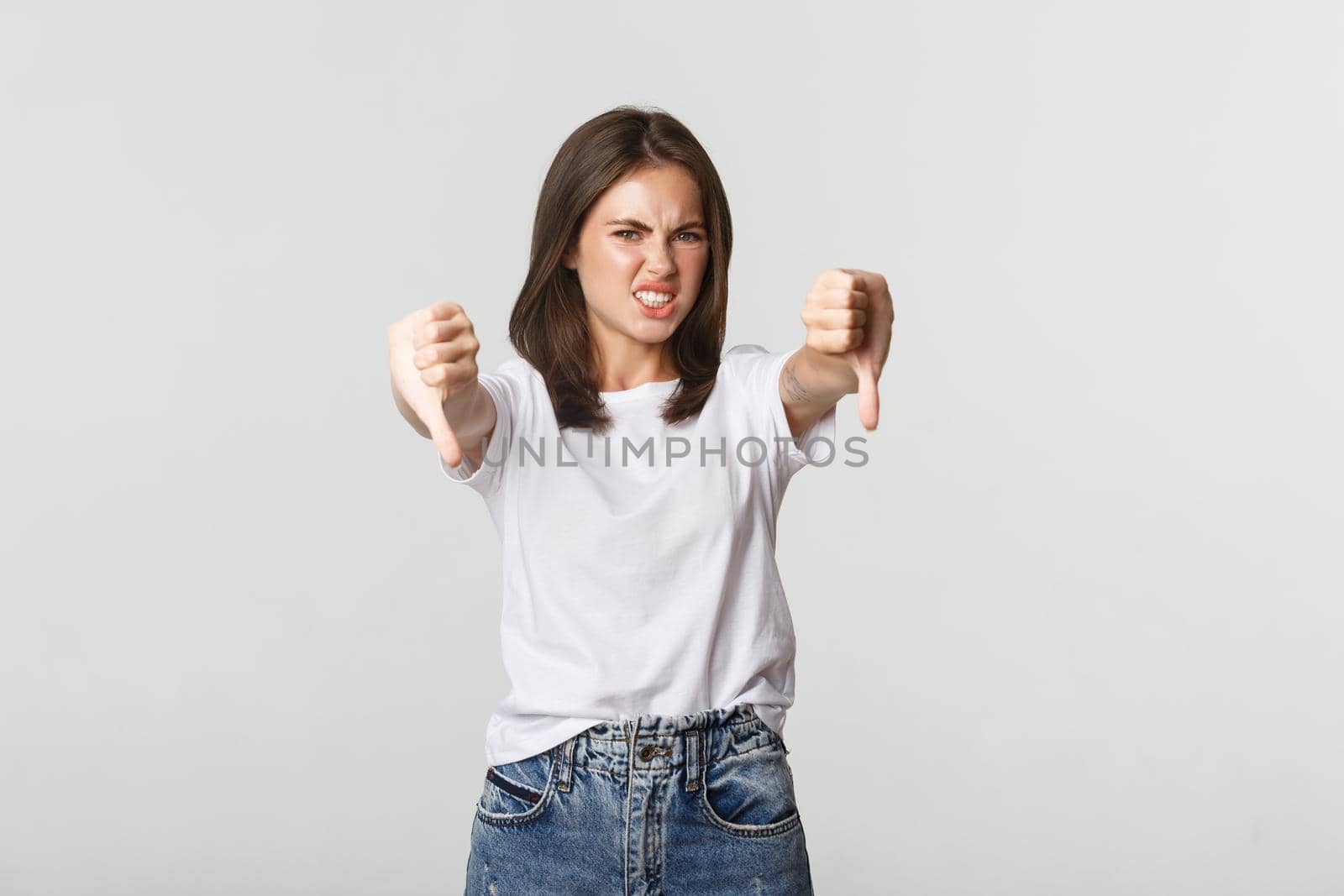 Disgusted brunette girl grimacing from dislike and showing thumbs-down.