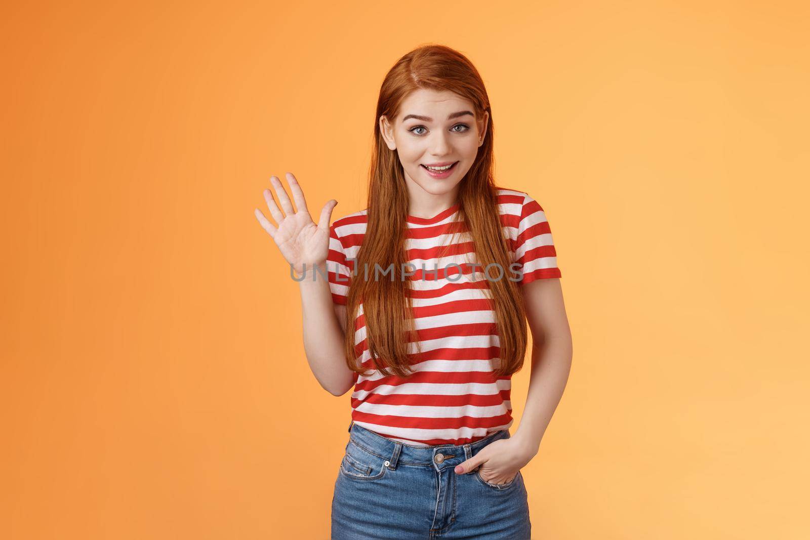 Hello how are you. Cute modest redhead newbie student female say hi, waving hand friendly, get know coworkers, smiling joyfully, introduce herself, welcome home, stand orange background by Benzoix