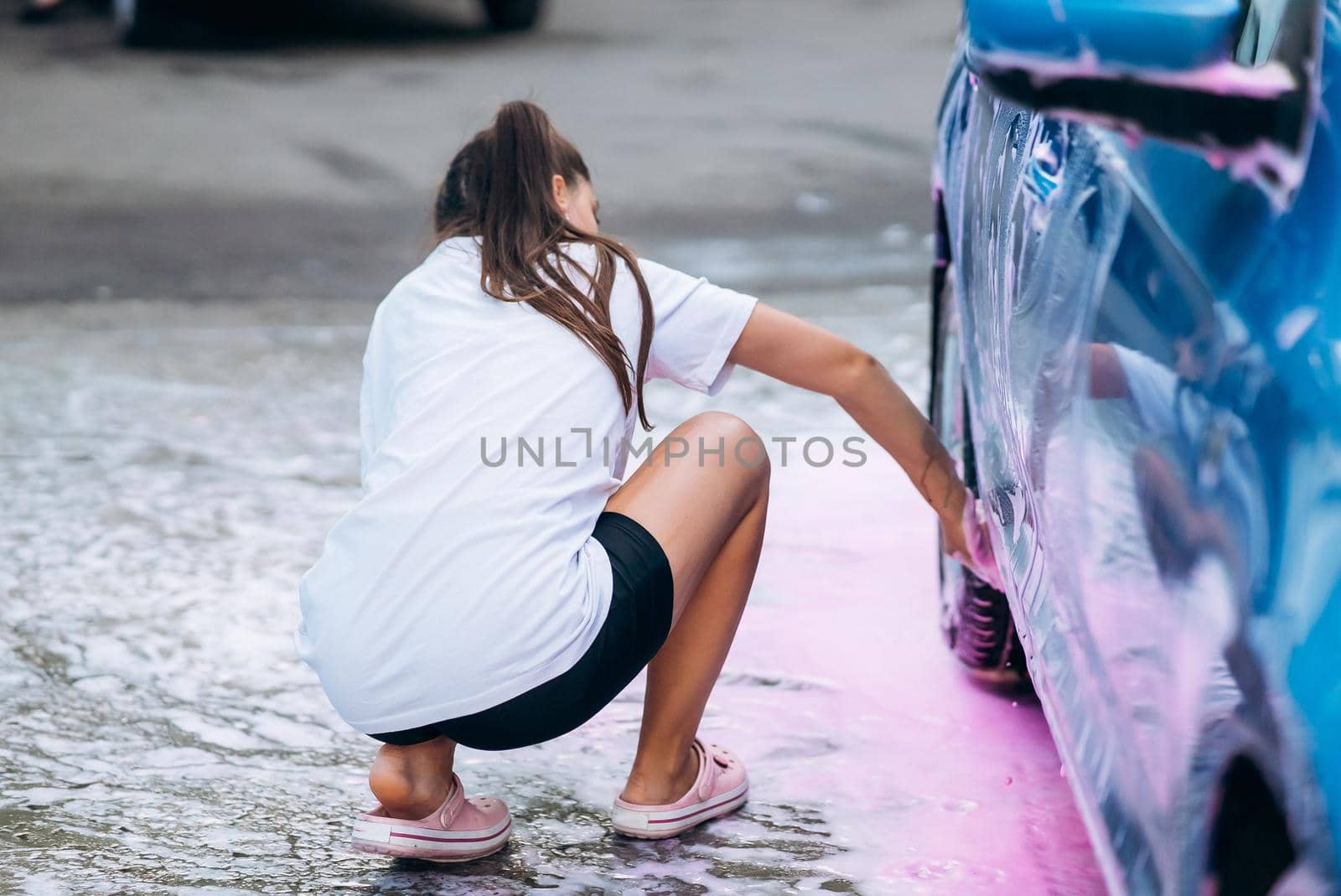 Woman with two pigtails with a sponge washes the side of the car