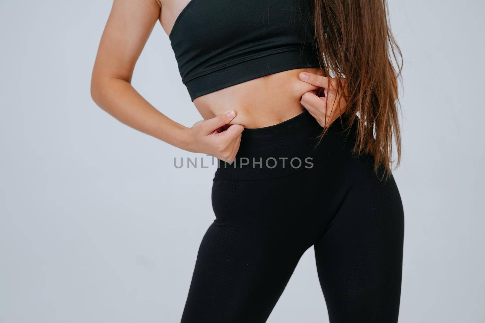 Young woman showing fat on her belly over white background. Lifestyle, sport, diet concept.