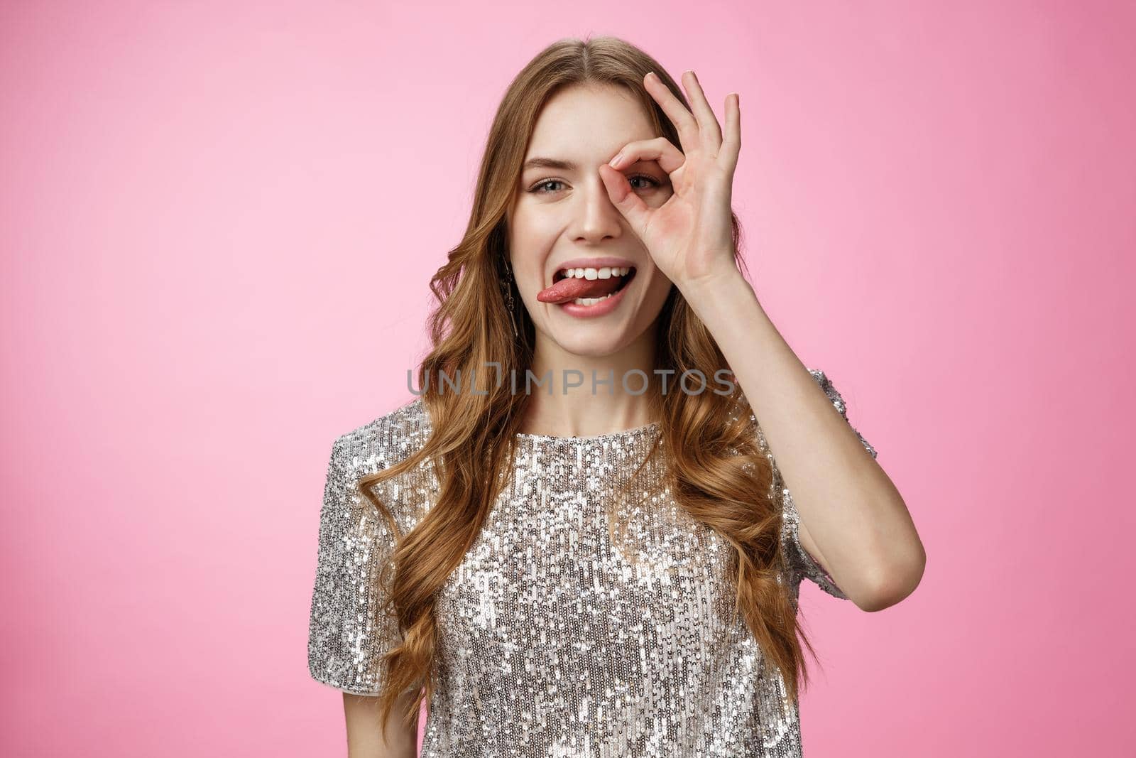 Playful carefree attractive funny caucasian fair-haired girl show tongue circle on eye like everything standing positive attitude enjoying life, make okay ok gesture, fooling around pink background.