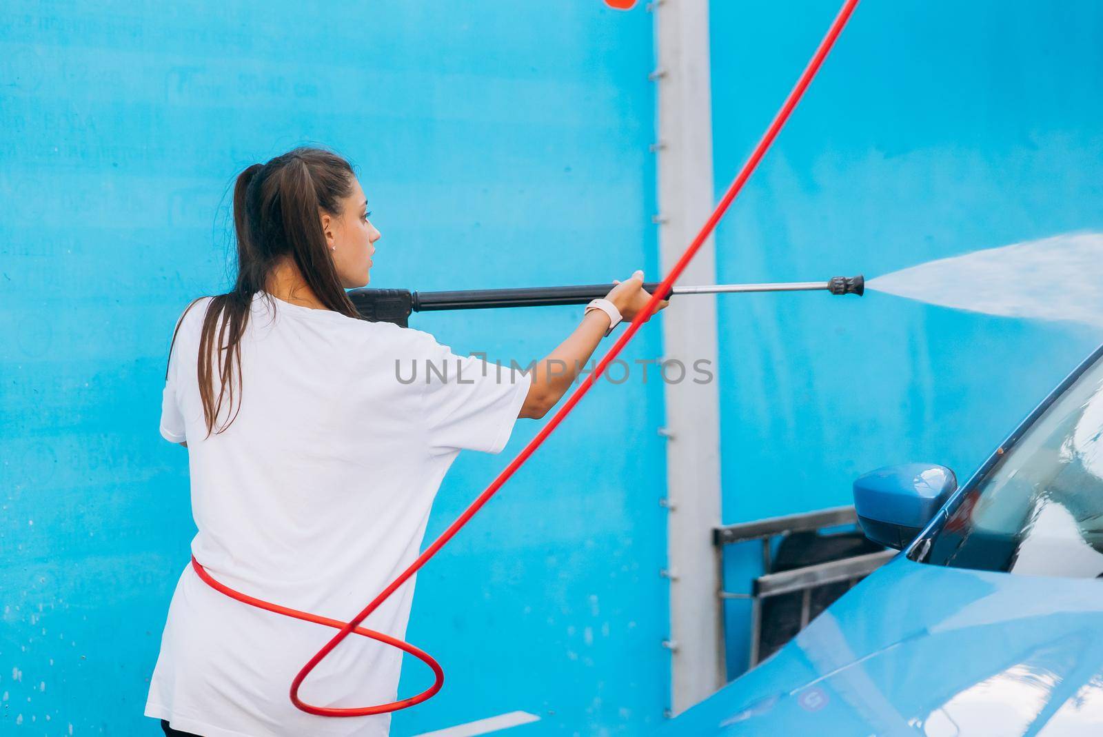 Brunette with two pigtails from a high-pressure hose washes the car at a car wash