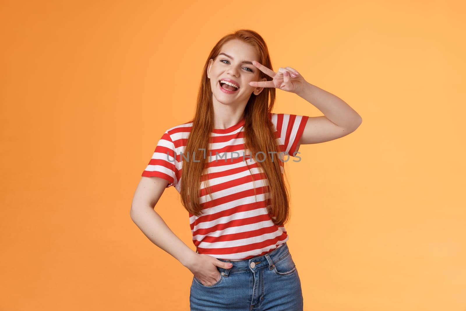 Friendly attractive modern redhead female college star show peace victory sign near eye, smiling happily, express positivity, joy and confidence, motivated win, stand orange background optimistic by Benzoix