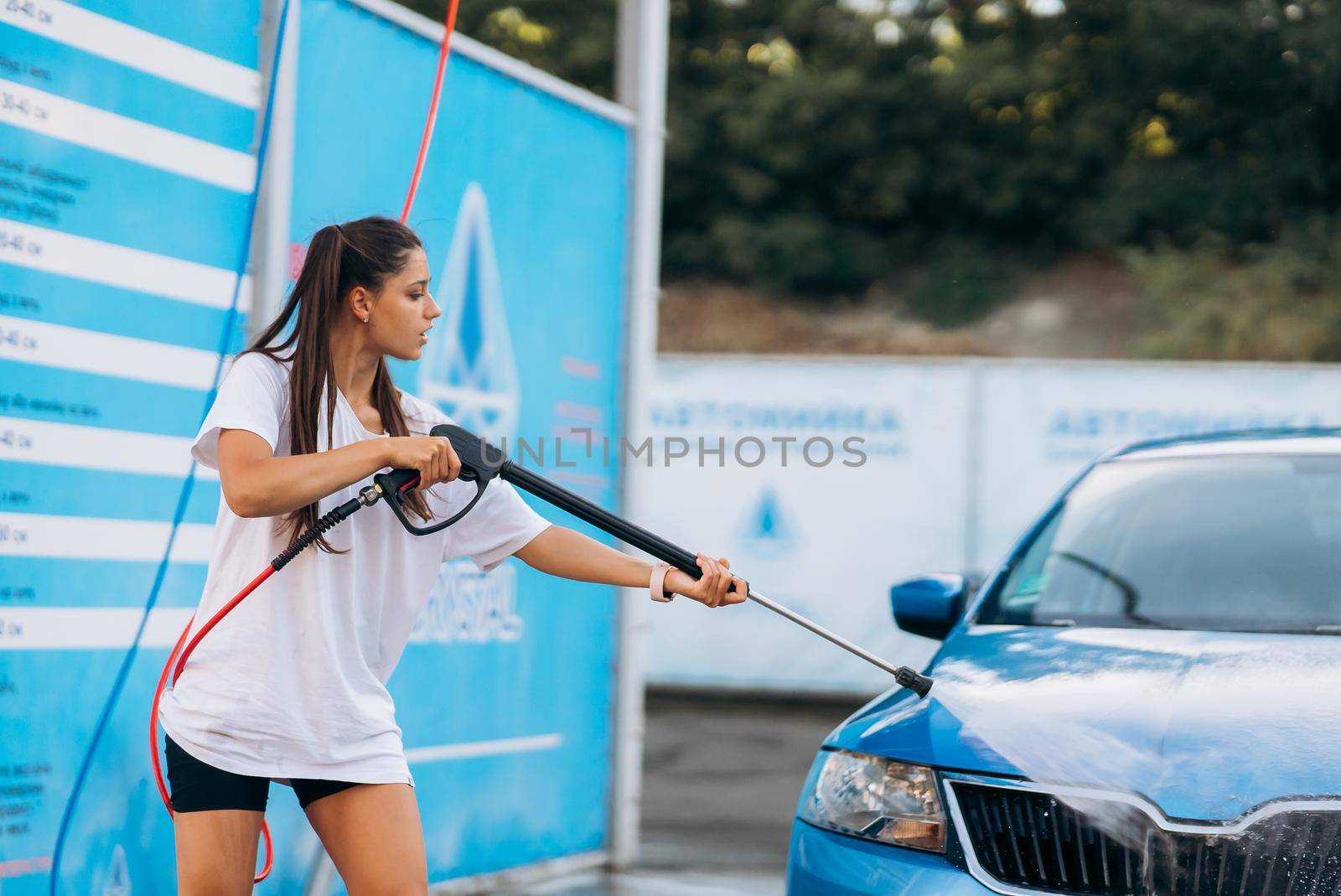 Brunette with two pigtails from a high-pressure hose washes the car at a car wash