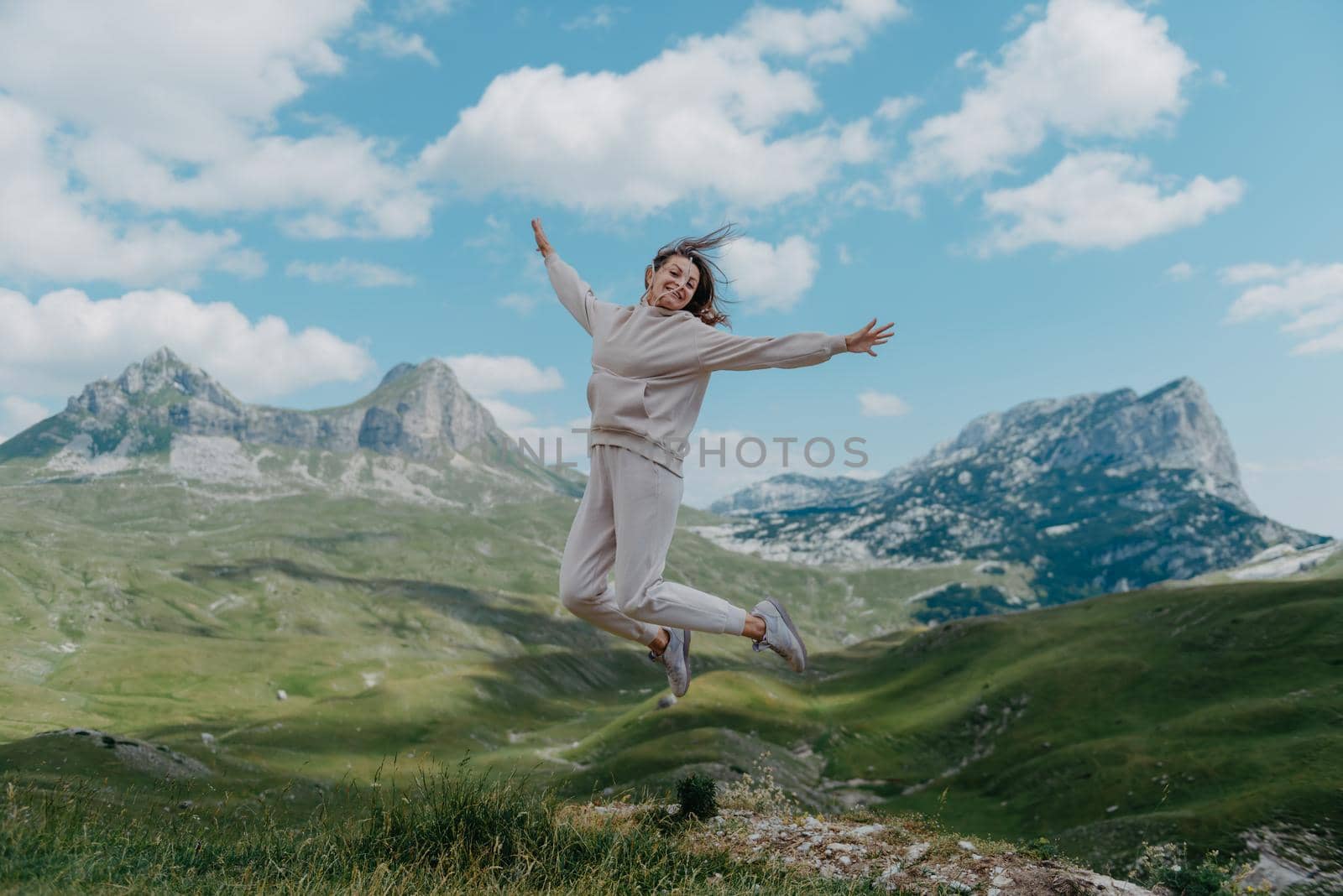 Happy pretty girl jumping high in the mountains. Young women joyfully jumping with mountain in background.