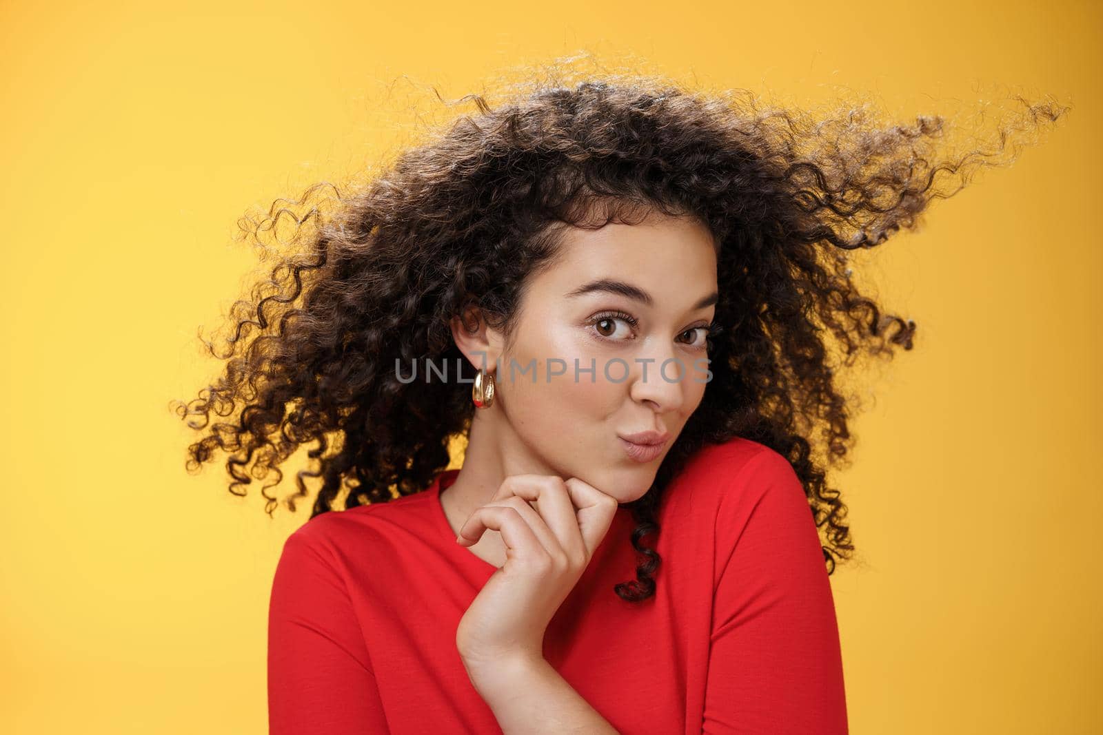 Cute flirty and silly female making coquettish gazed at camera folding lips feminine turning head and touching chin as seducing while hair curls waving in air expressing foreplay and romantic attitude.