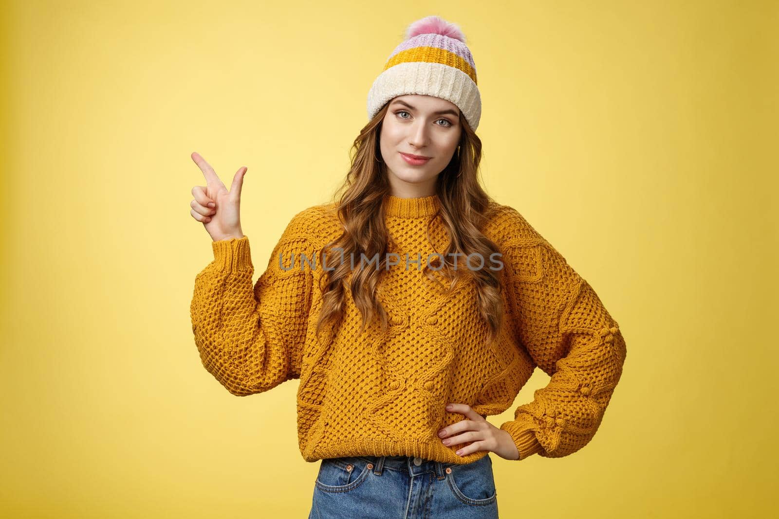 Confident good-looking young female friend telling you buy product immidietely pointing upper left corner smiling hold hand waist self-assured, employee help client pick best merch, yellow background.