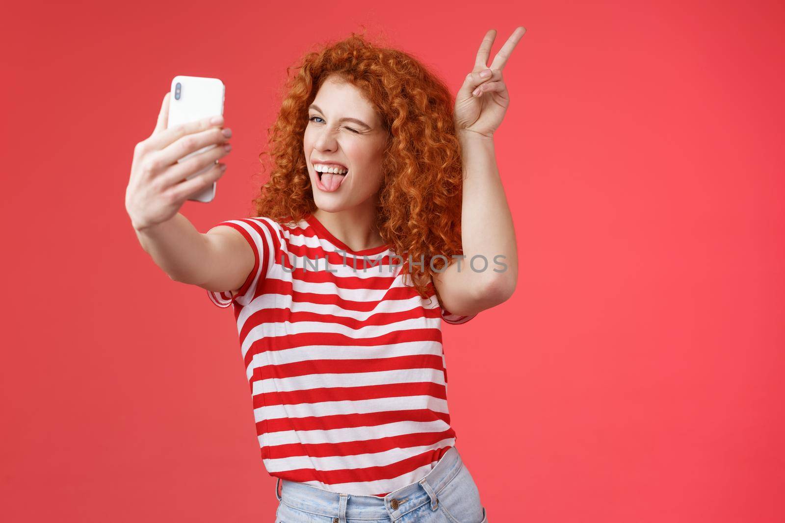 Sassy fashionable playful good-looking redhead daring curly woman show peace victory animal ears gesture winking smartphone display record vlog taking selfie awesome phone camera red background.
