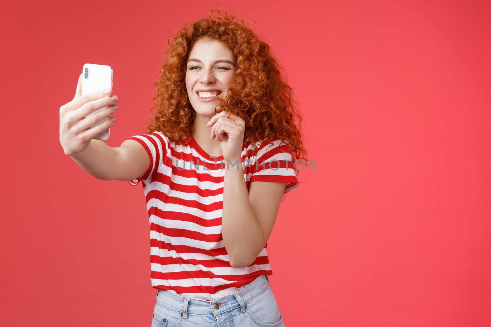 Sassy good-looking stylish charismatic redhead female curly hairstyle winking cheeky expression making flirty kinky faces hold smartphone taking selfie record video message play funny facial filters by Benzoix