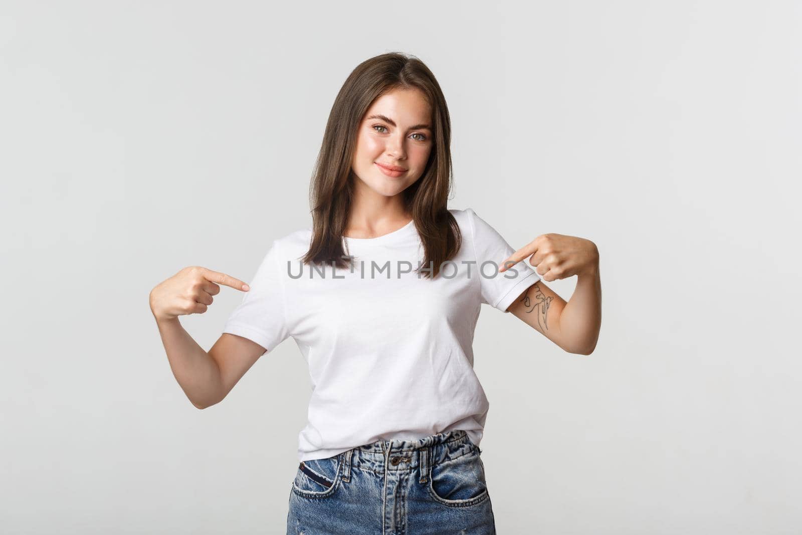 Beautiful smiling brunette girl pointing fingers at your logo, showing something on center.