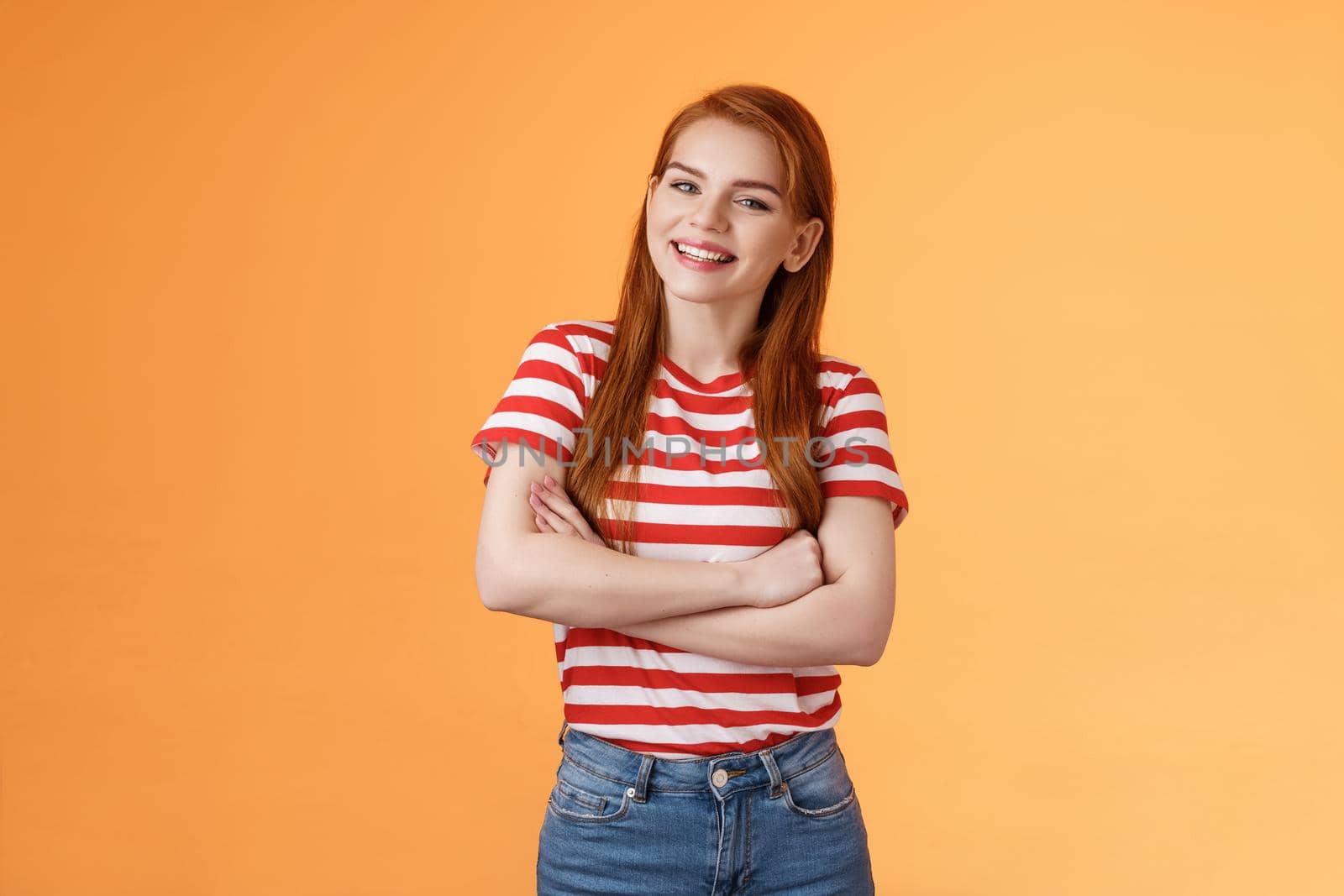 Cheerful cute redhead 20s girl cross arms smiling broadly, lively talking friend, grinning keep conversation, stand orange background delighted, feel fine, wear casual t-shirt jeans.