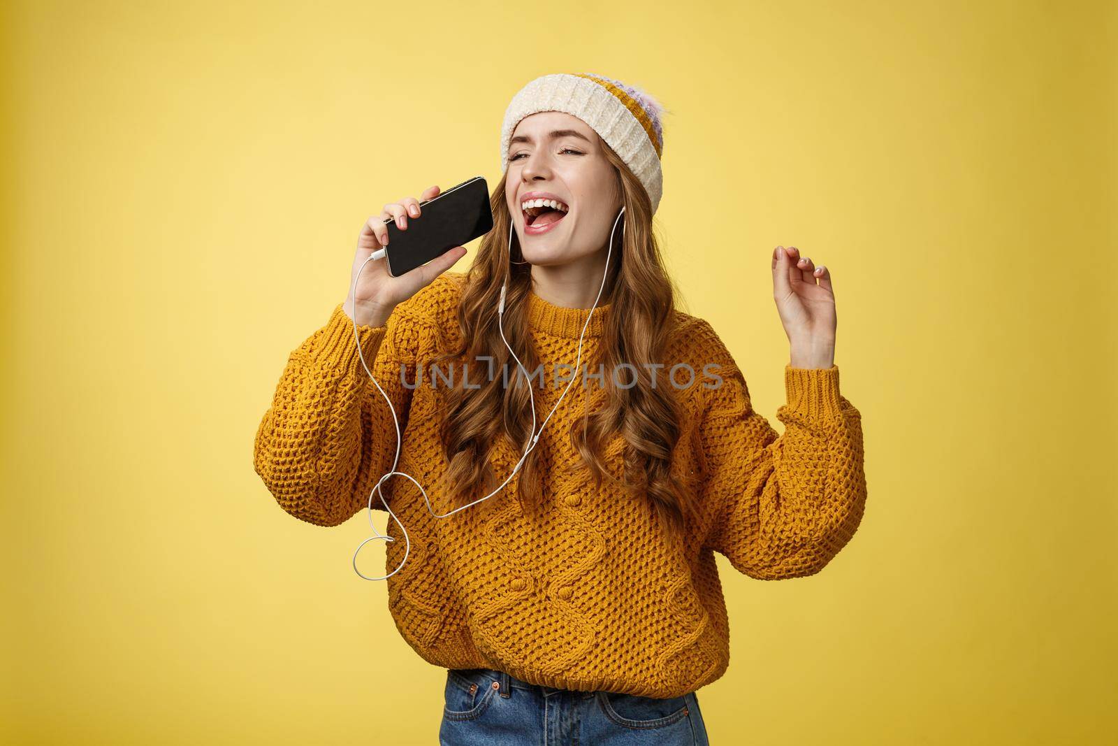 Carefree charming girl likes karaoke having fun listen favorite songs wearing wired earphones hold smartphone microphone singing out loud dancing enjoying spend time alone. Technology concept