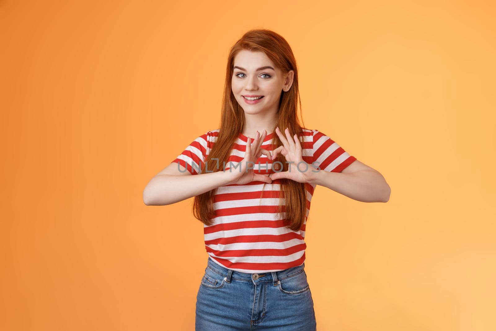 Cute lovely cheerful redhead girlfriend express love and cherish relationship, celebrating anniversary show heart sign, smiling tenderly, confess sympathy, stand orange background by Benzoix
