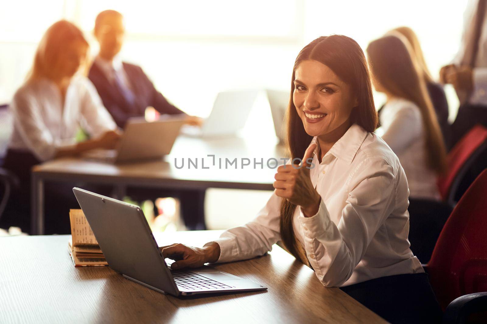 Cheerful young freelance woman working on laptop sitting at the open space office or coworking. Working woman working on a business proposal or developing IT applications. Toned image.