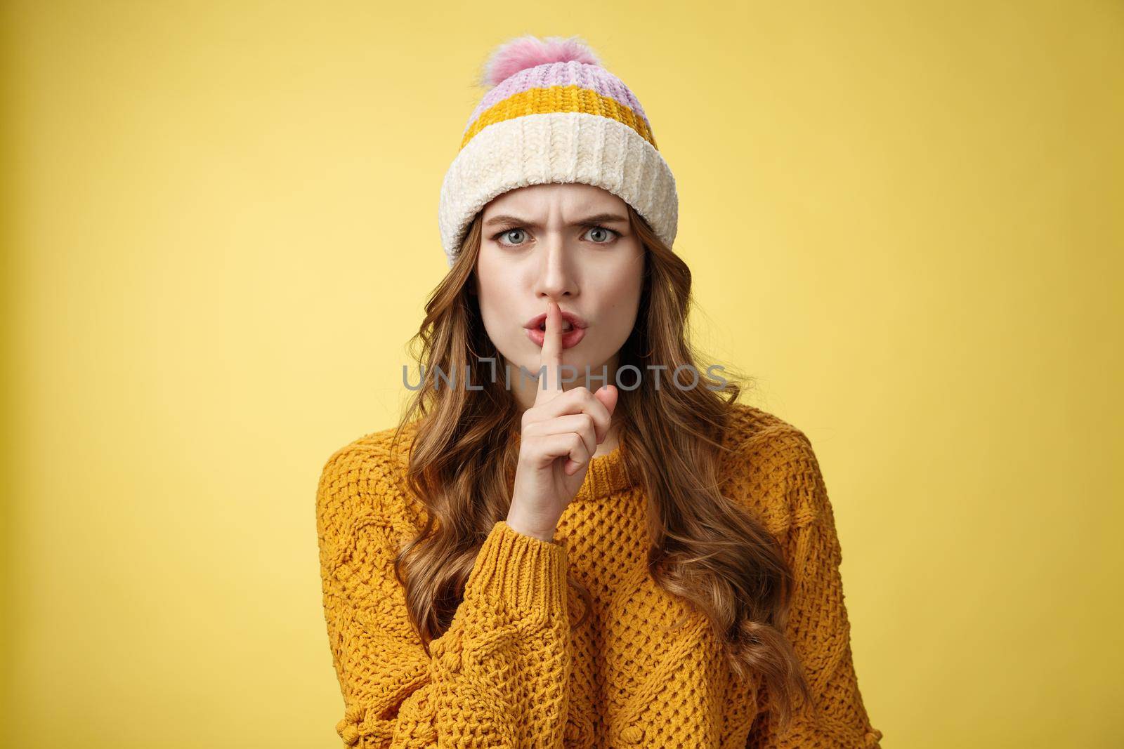 Furious angry annoyed cute woman shushing you irritated loud talk during important meeting frowning cringing pissed showing shhh gesture index finger pressed mouth, yellow background.