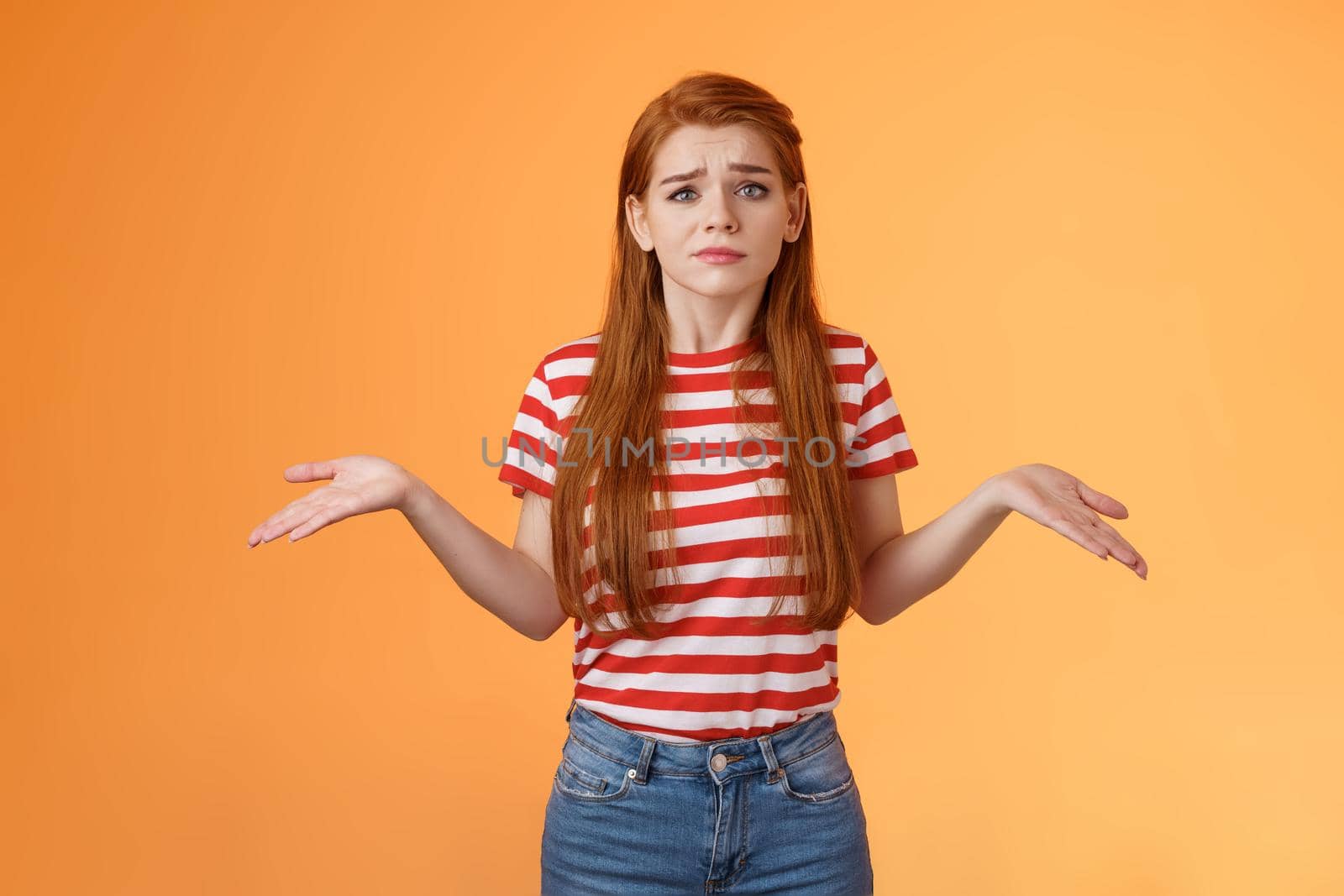 Uneasy questioned and clueless lovely modern stylish redhead woman shrugging spread hands sideways unaware, grimacing perplexed, tough question, have no answer, stand orange background by Benzoix