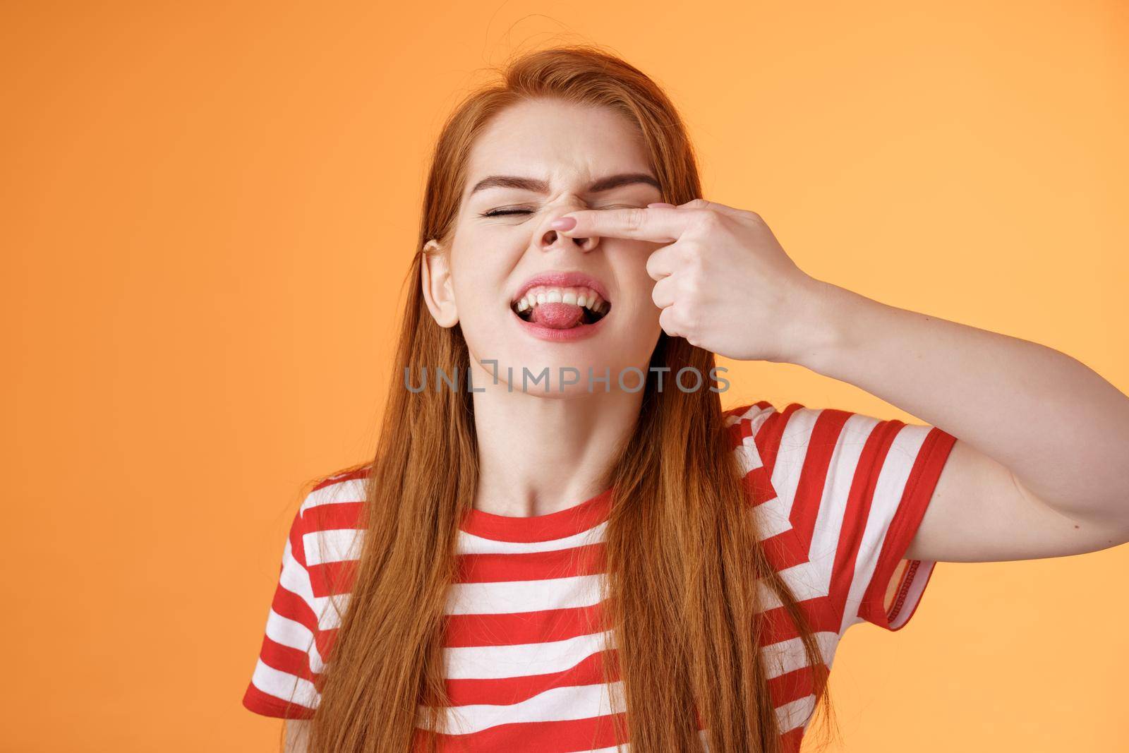 Silly childish redhead girl fool around, make piggy nose, show tongue immature carefree, having fun, playful enthusiastic mood, stand upbeat show nostrils happily grinning, orange background.