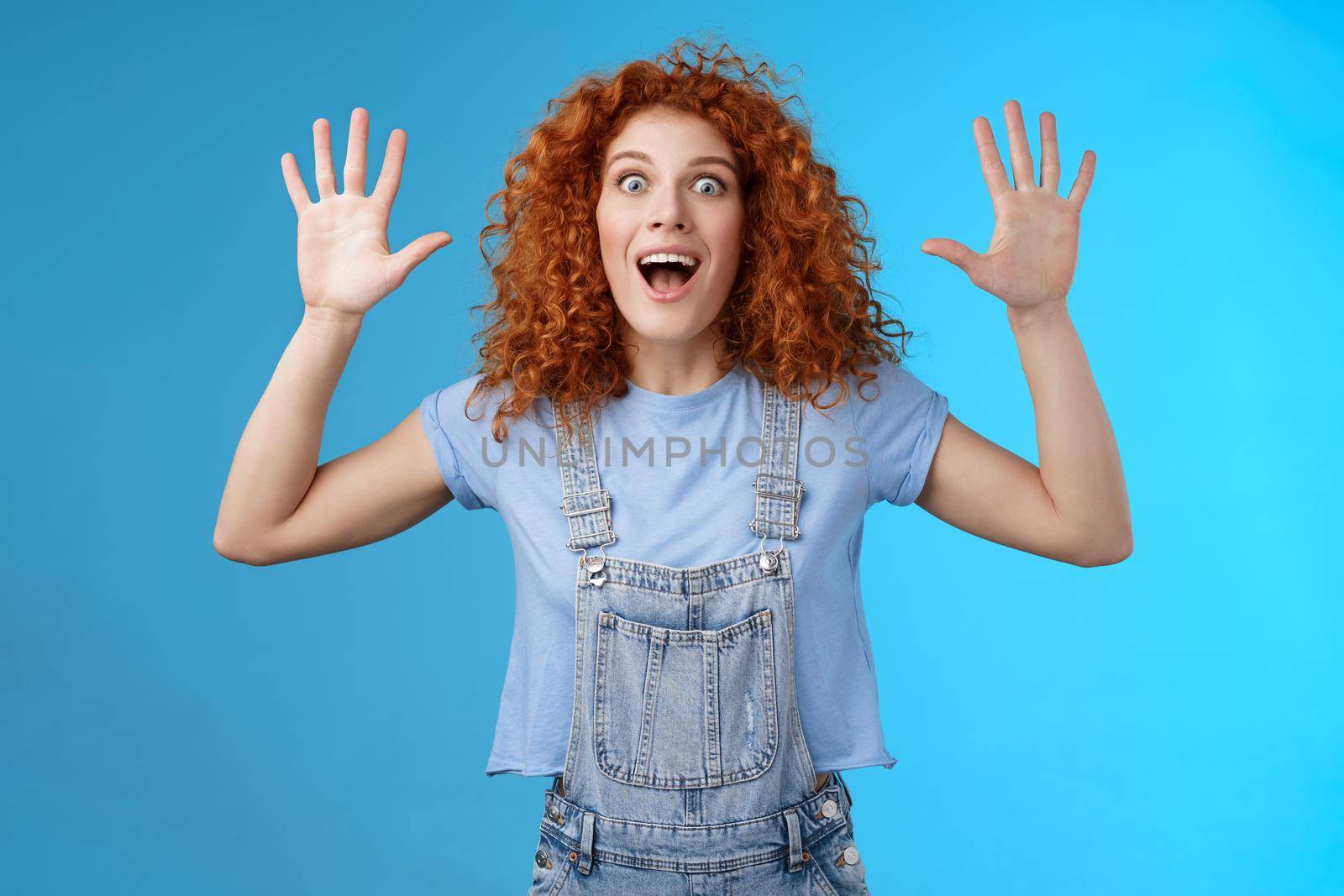Excited crazy playful funny redhead curly emotive girl yelling carefree raise hands surrender up open mouth fool around smiling broadly stare camera joyful express wild daring emotions.