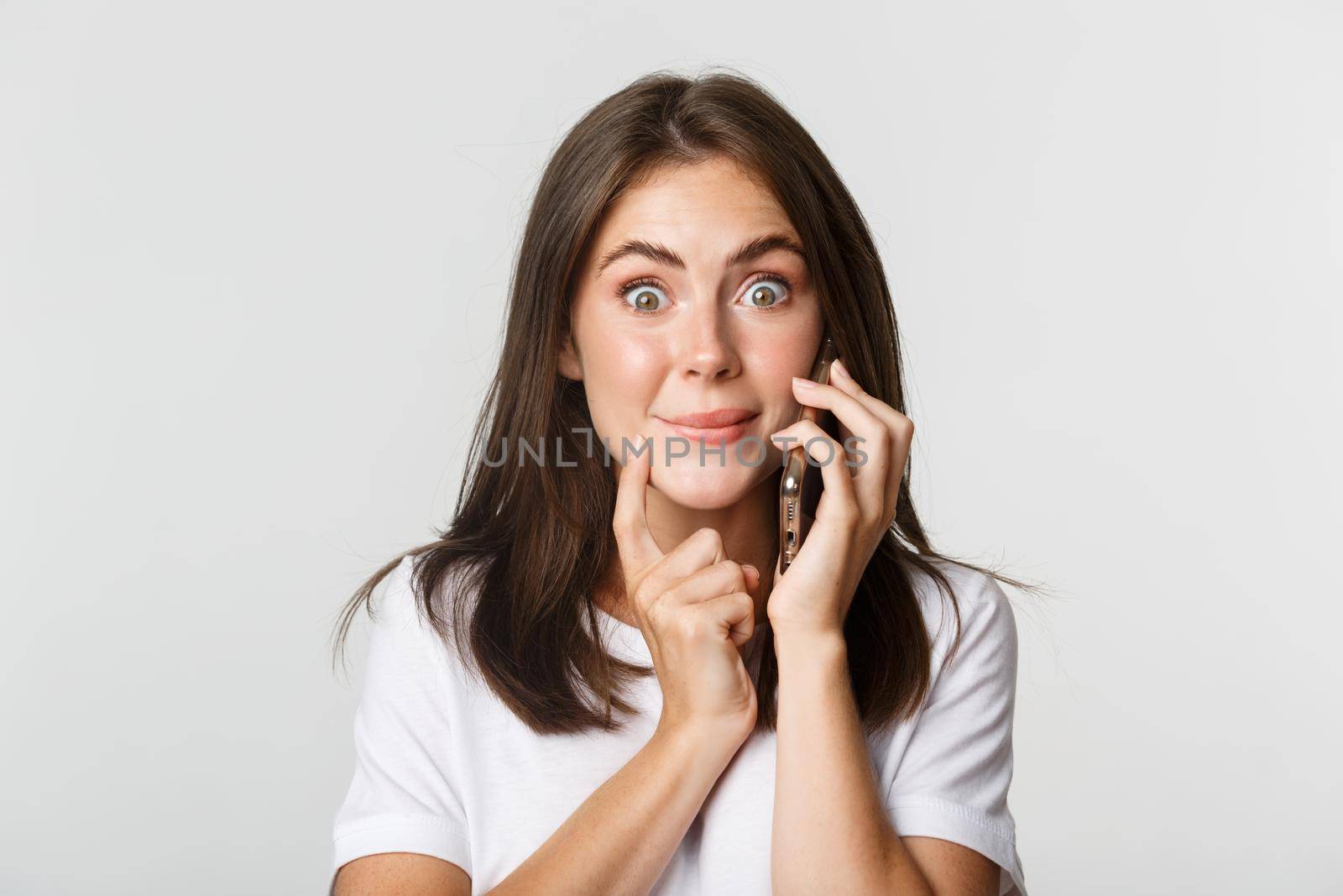 Close-up of intrigued smiling girl talking on smartphone with tempted expression.