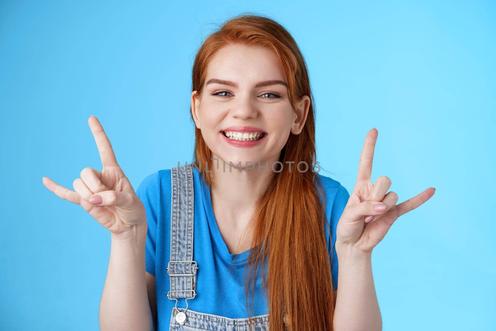 Close-up cheerful lucky joyful redhead woman having fun, enjoying summertime, show rock-n-roll gesture attend awesome party concert, make heavy-metal sign and smiling blue background.