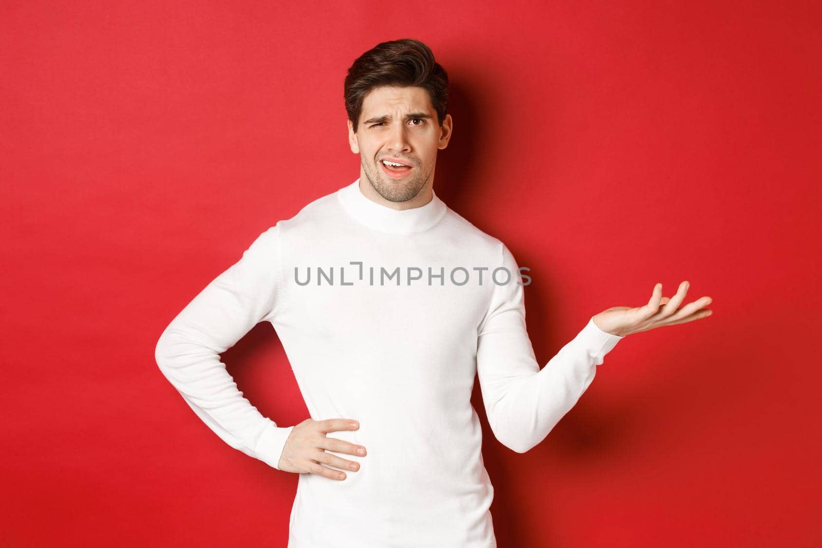 Portrait of confused and displeased man, complaining about something, looking with dismay, standing over red background.