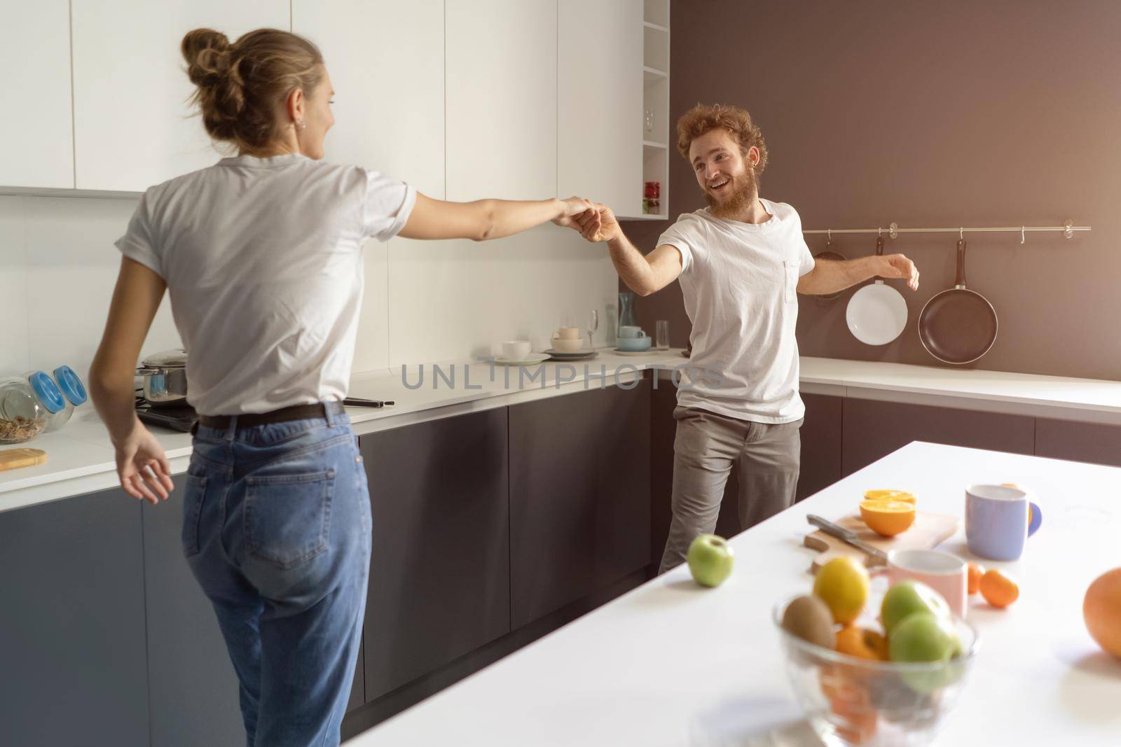 Waltzing in a new home young couple dancing celebrating their new purchase of buying their own house. Happy new family at kitchen wearing casual clothes. Love, family, happiness concept.