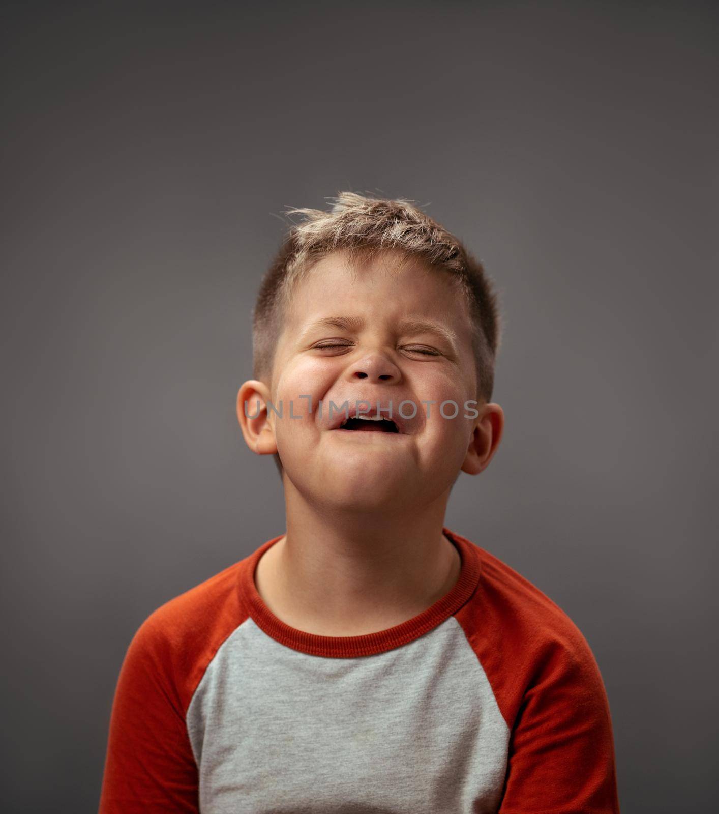 Portrait of a sad pretending cry little boy isolated on grey background. Fake emotions. Human emotions, facial expression concept. Facial expressions, emotions, feelings.