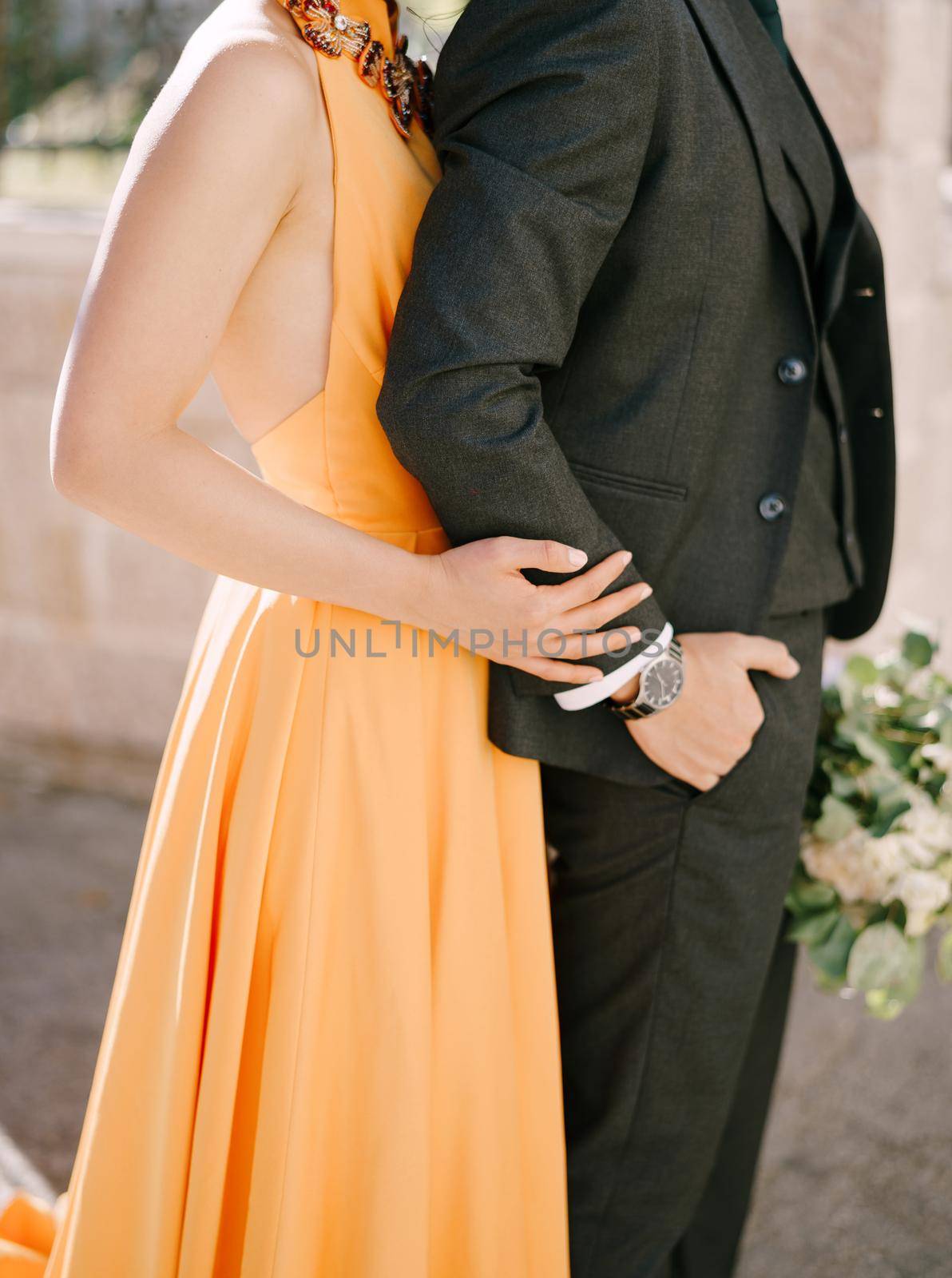 Woman in a yellow dress hugs man from behind with a bouquet. Close-up by Nadtochiy