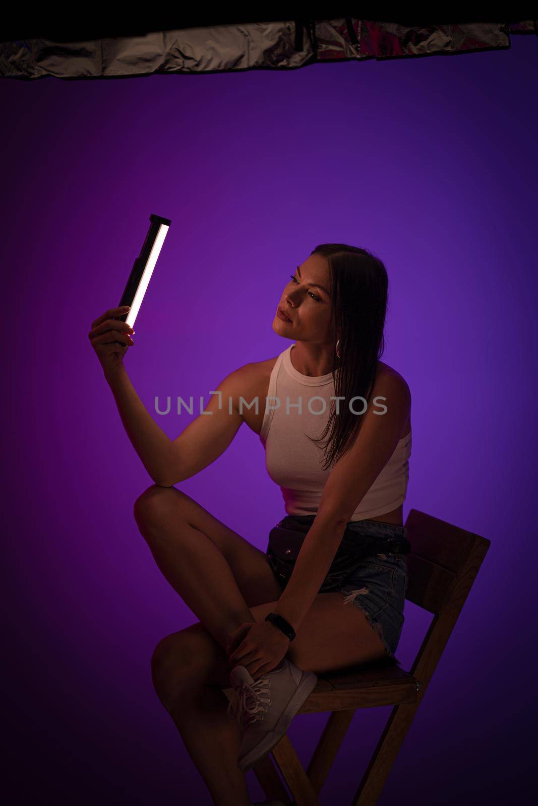 Woman holds LED lamp looking on it against of purple background. Presentation of Nanlite Studio Lighting. Backstage concept. June 2020, Kiev Ukraine.