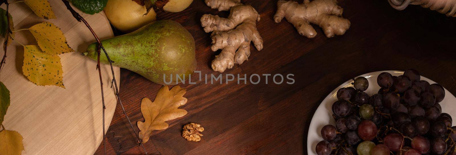 Panoramic banner. Close up top view of a fruits, grapes, ginger root on a wooden table. Wine snacks set: selection of cheese, grapes, pear and walnuts on a wooden board by LipikStockMedia
