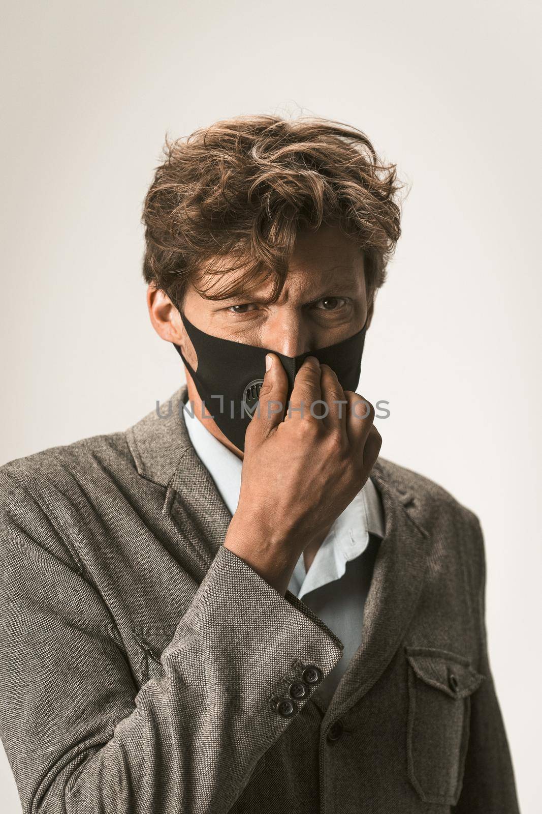 Close up portrait of young business man in a disposable facial mask in grey jacket and a modern reusable protective mask on his face fixing it. Epidemic concept. Coronavirus epidemic by LipikStockMedia