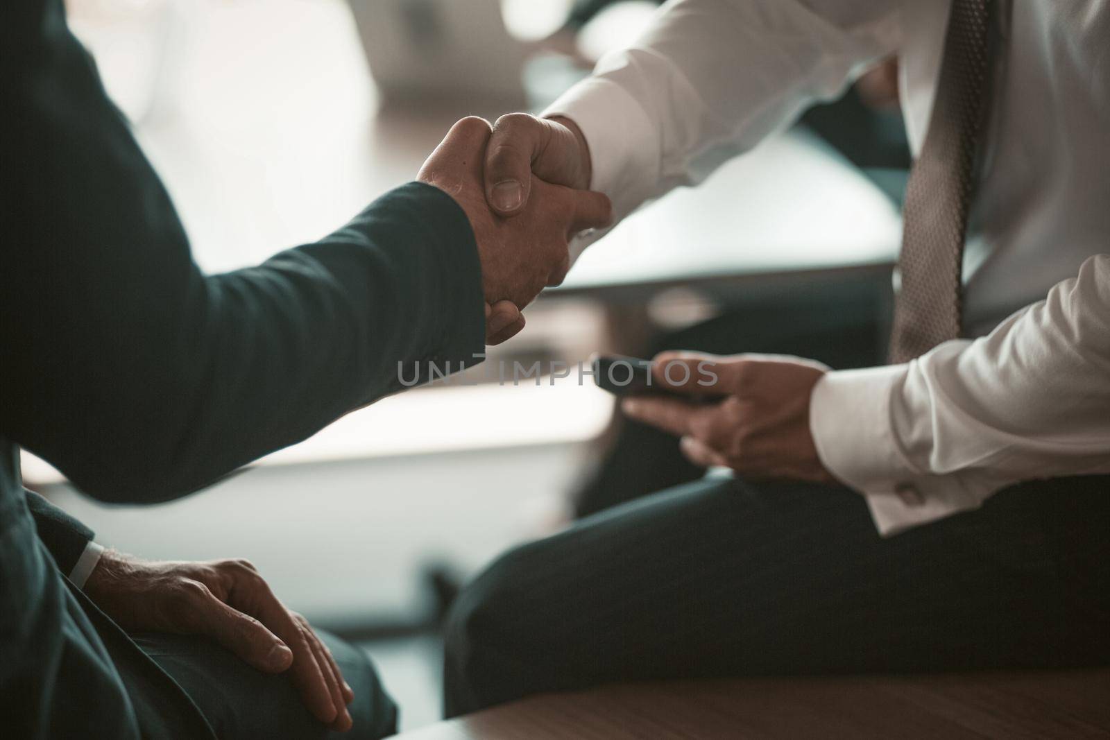 Two businessmen handshaking colleagues or business partners on modern office background. Business concept. Close up shot.