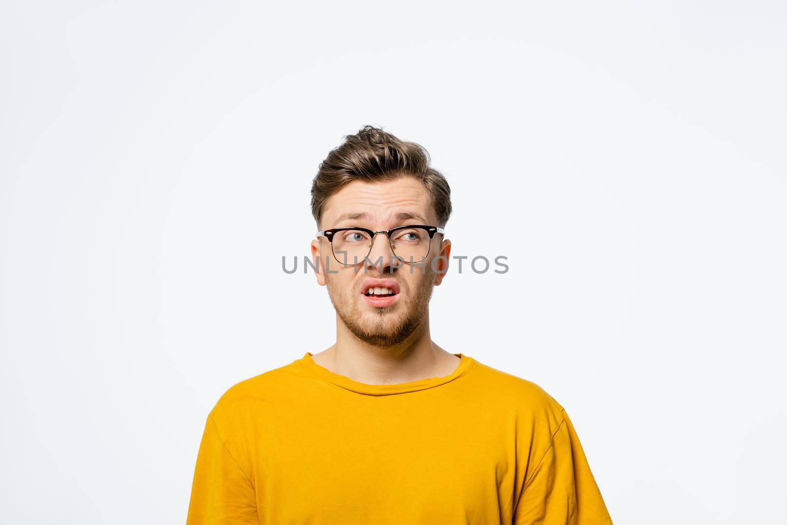 Handsome young man in eye glasses shocked with surprise expression, fear and excited on his face.Young casual man portrait isolated on yellow background.