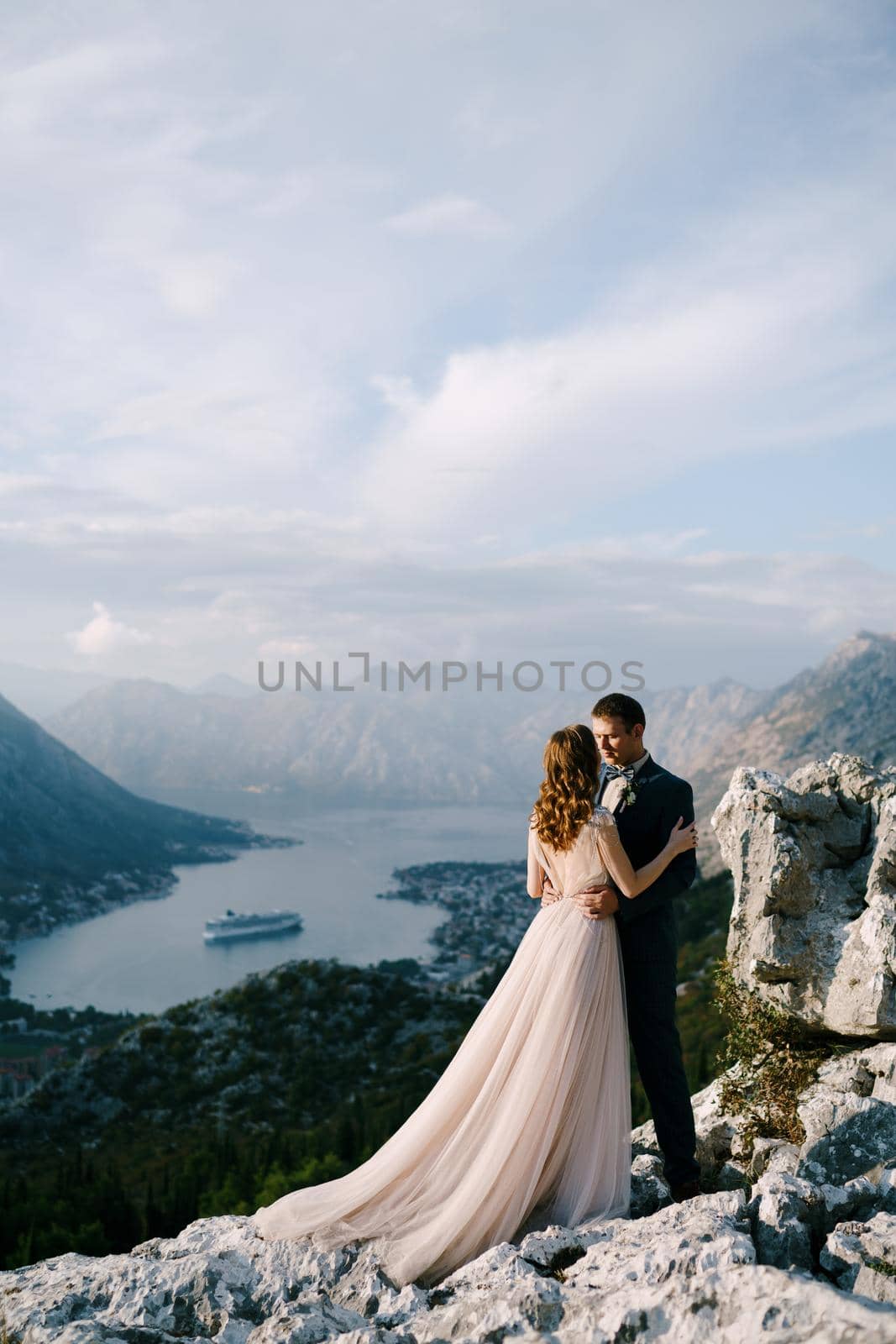 Groom hugs bride by the waist on a rocky mountain overlooking the bay. High quality photo