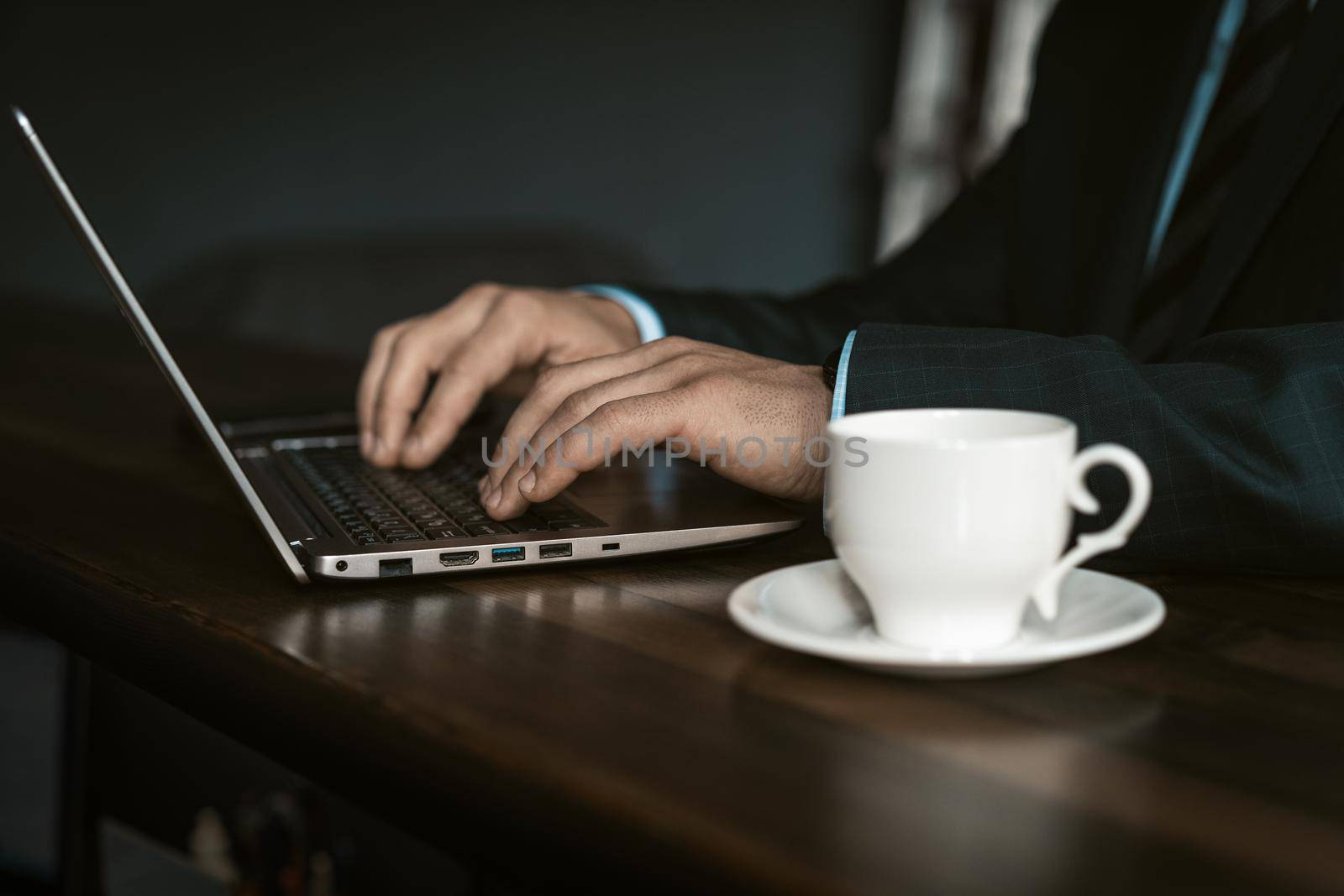 Close up professional businessman working on laptop and drinking cup of coffee sitting at the modern office. Man working on laptop in office. Business and finance concept.