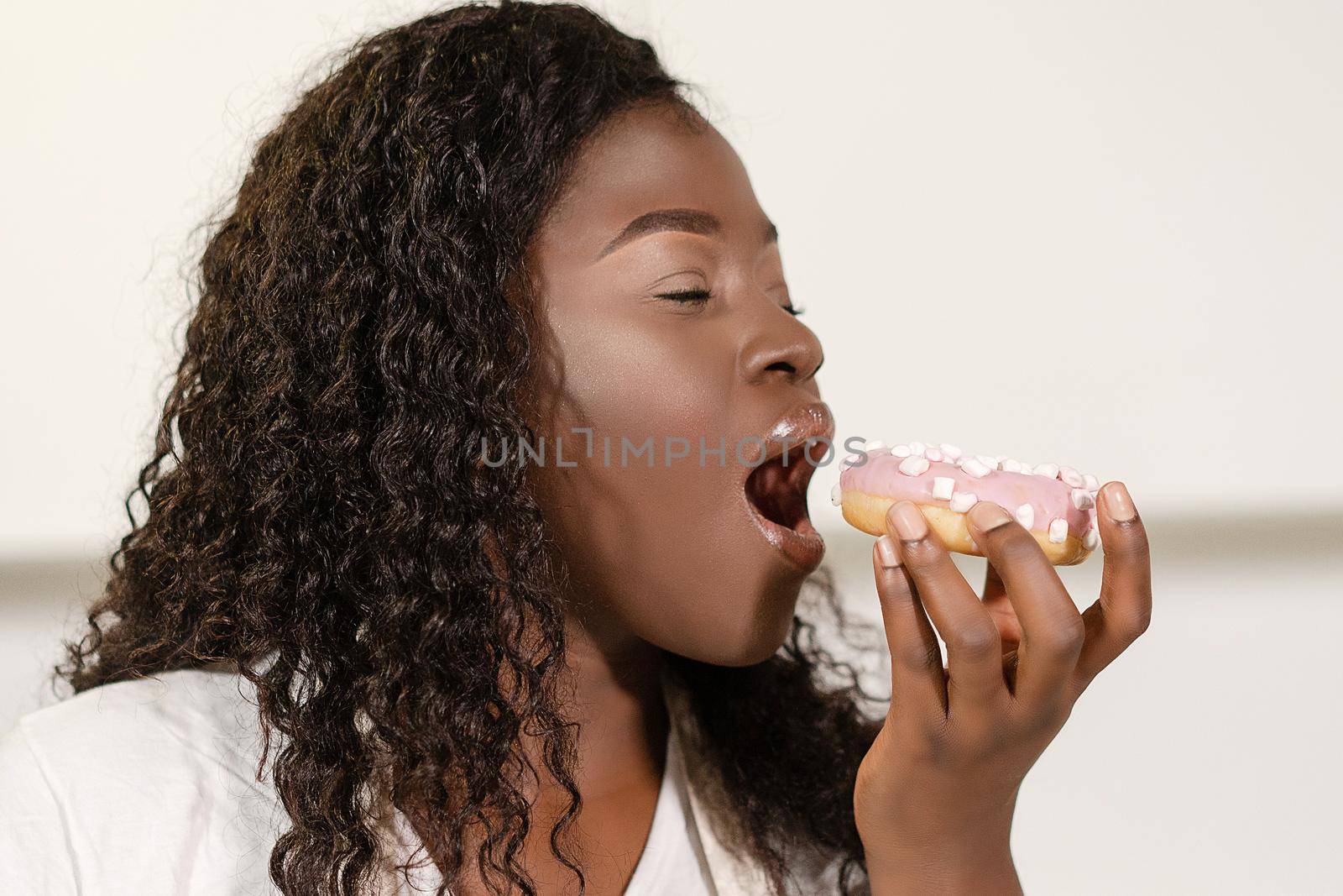 Afro Young Woman Biting Pink Donut. Face Close-up. White Background. High quality photo