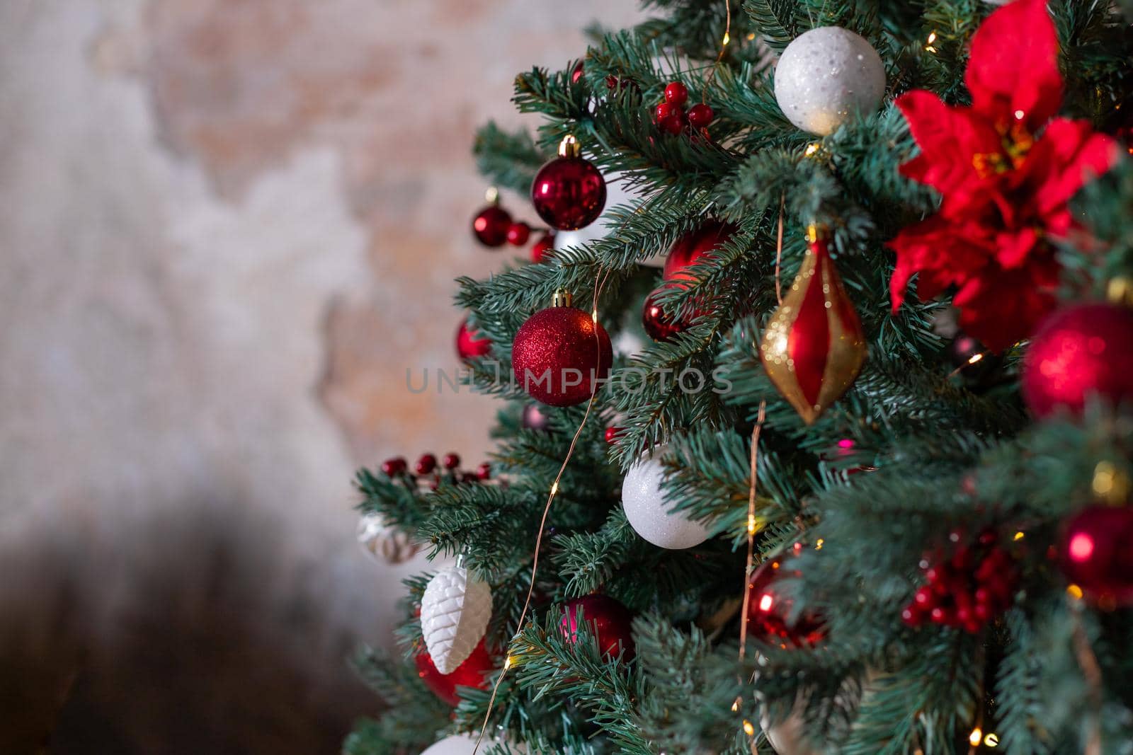 Closeup photo of red Christmas ball on fir tree next to fireplace