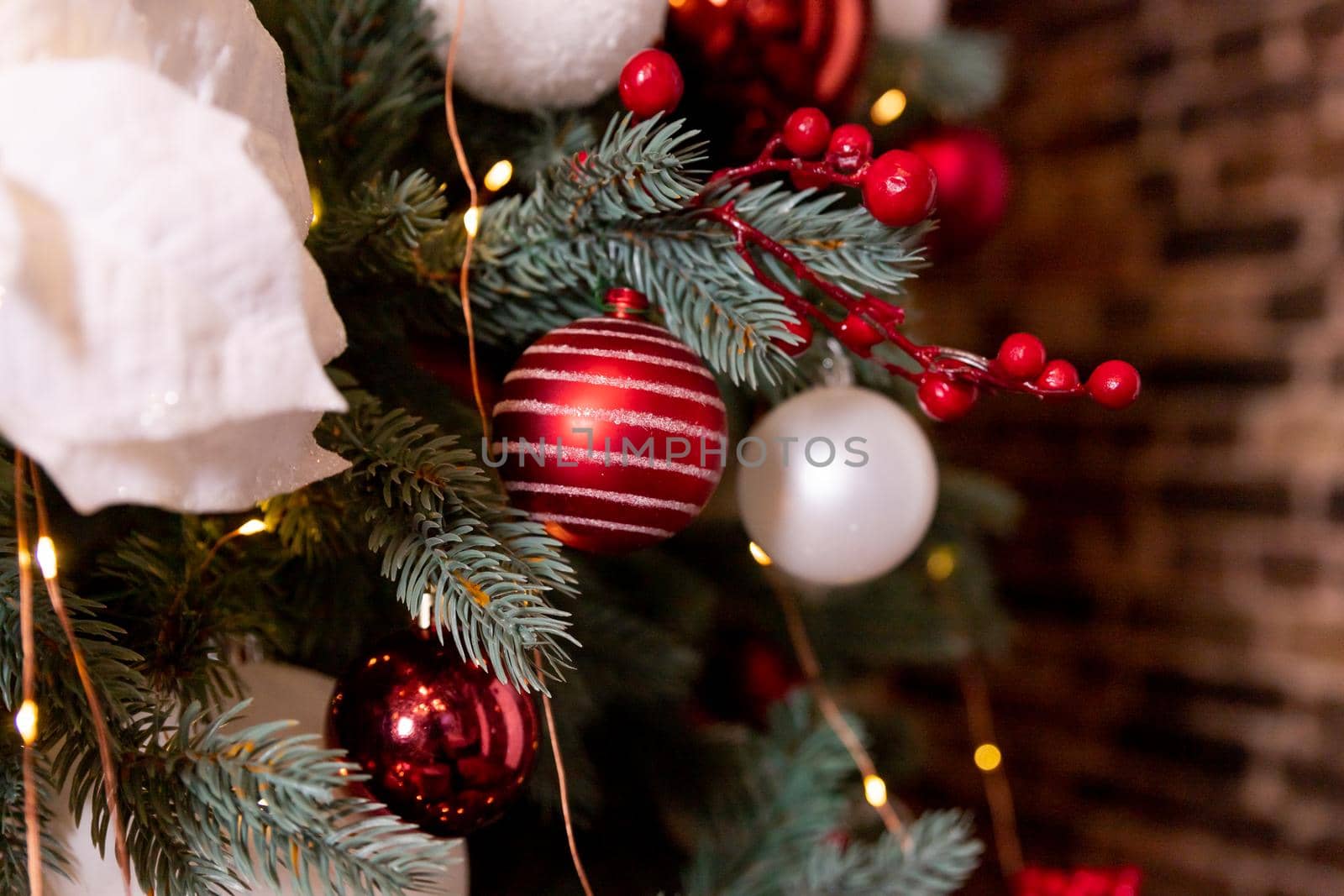 Closeup photo of red Christmas ball on fir tree next to fireplace