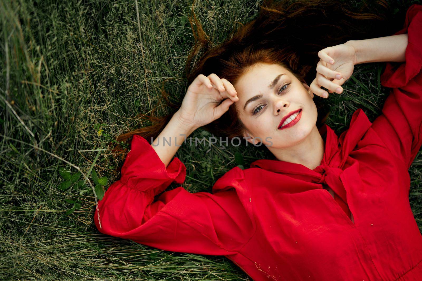 cheerful woman in a red dress lies on the grass top view. High quality photo