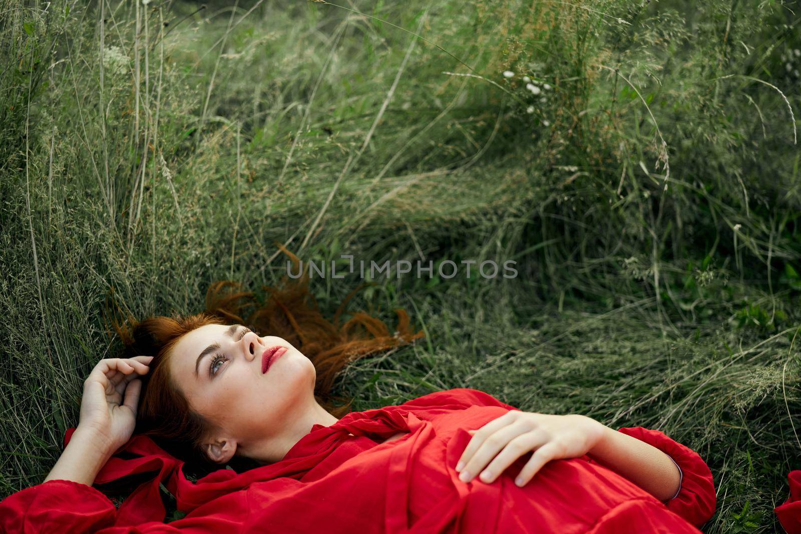 pretty woman in red dress lies on the grass freedom landscape. High quality photo