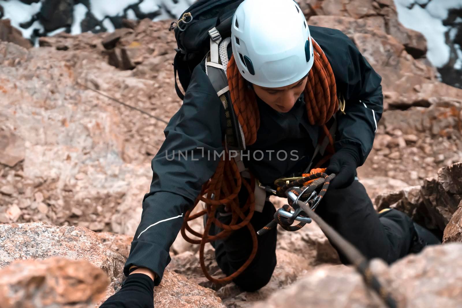 A young man in a helmet and with climbing equipment descends from the top of the mountain on a rope, the climber rappels with aperture-style self-braking belay in the snowy mountains.