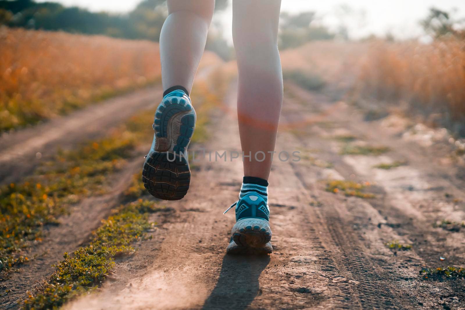 Female athletic legs in sneakers at sunset during outdoor jogging at sunset. A young girl warms up, is engaged in trail running, view on her legs closeup.