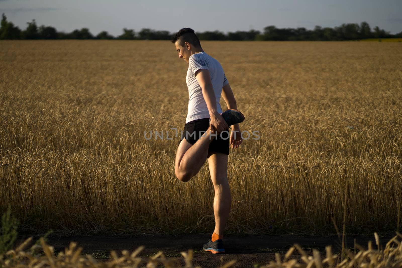 An athletic man jogging along the trails in a wheat field outside the city at sunset, a runner training in a picturesque outdoor area.