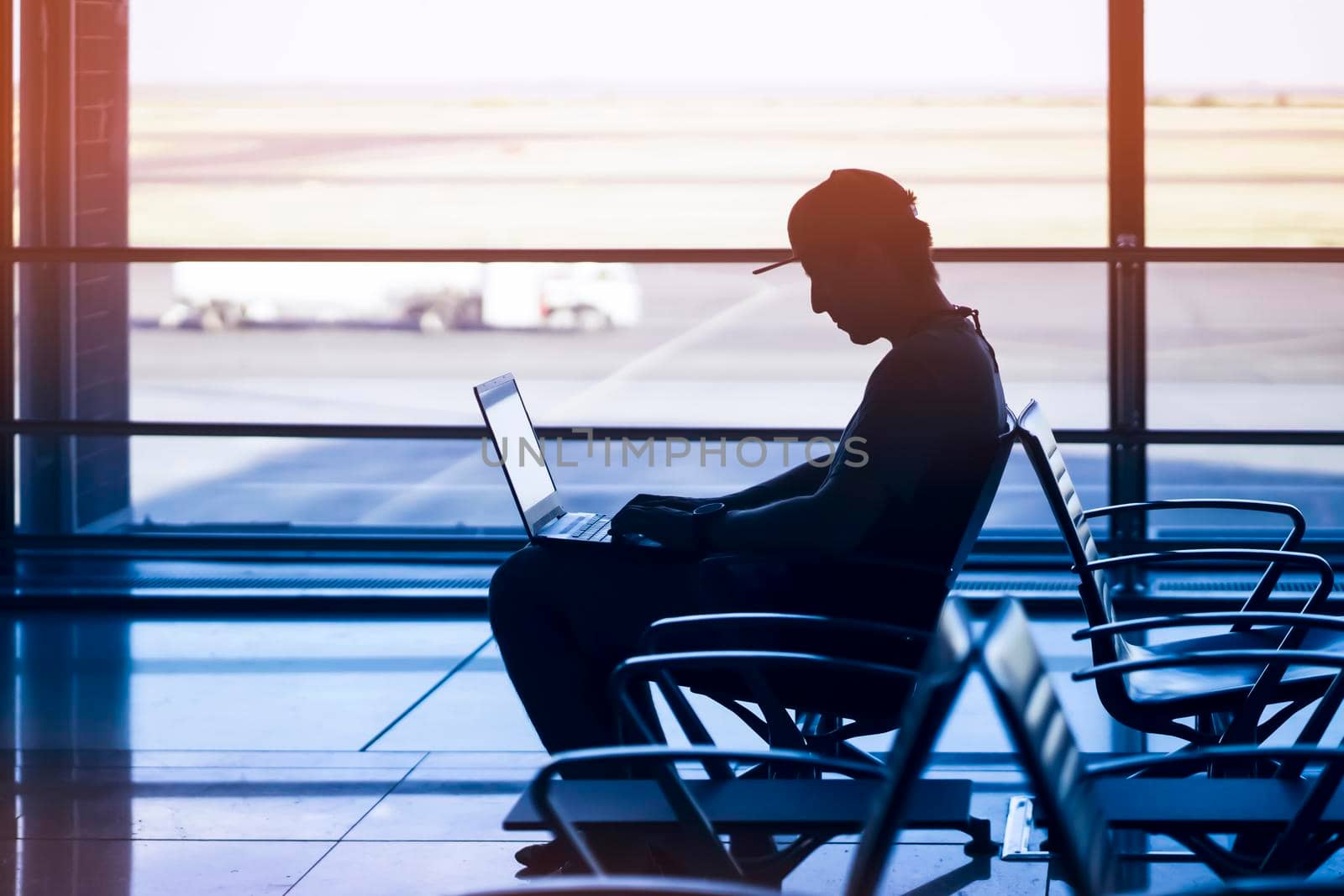 A young man is working on a laptop at the airport while waiting to board the plane. A man is engaged in business, buys tickets, studies and communicates via the Internet in the evening.